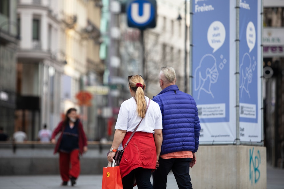 Menschen neben einen Plakat mit der Maskenpflicht am Stephansplatz im Zentrum von Wien.