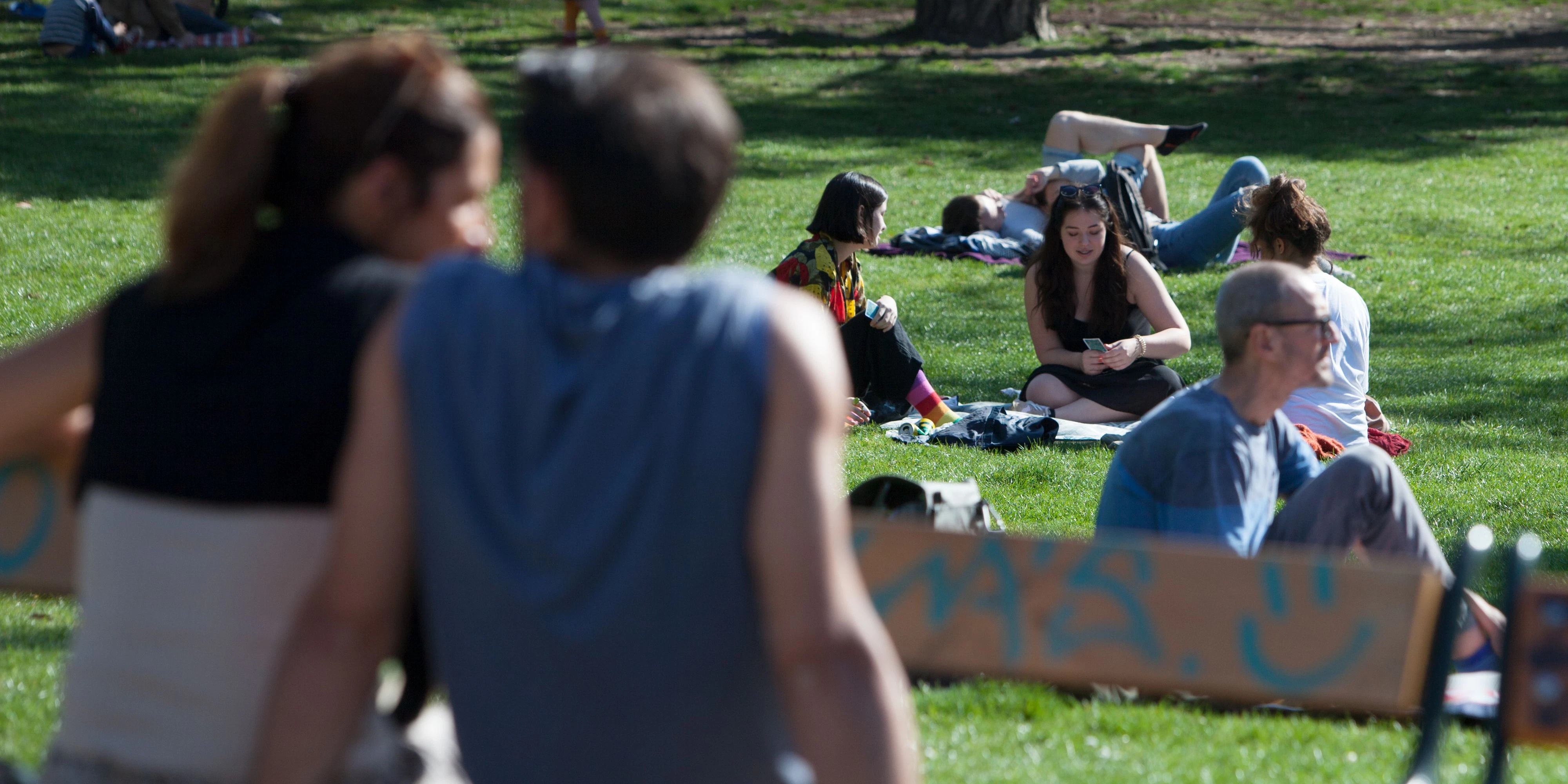 Menschen sitzen auf Bänken und am Rassen bei Sonnenschein im Stadtpark in Wien.