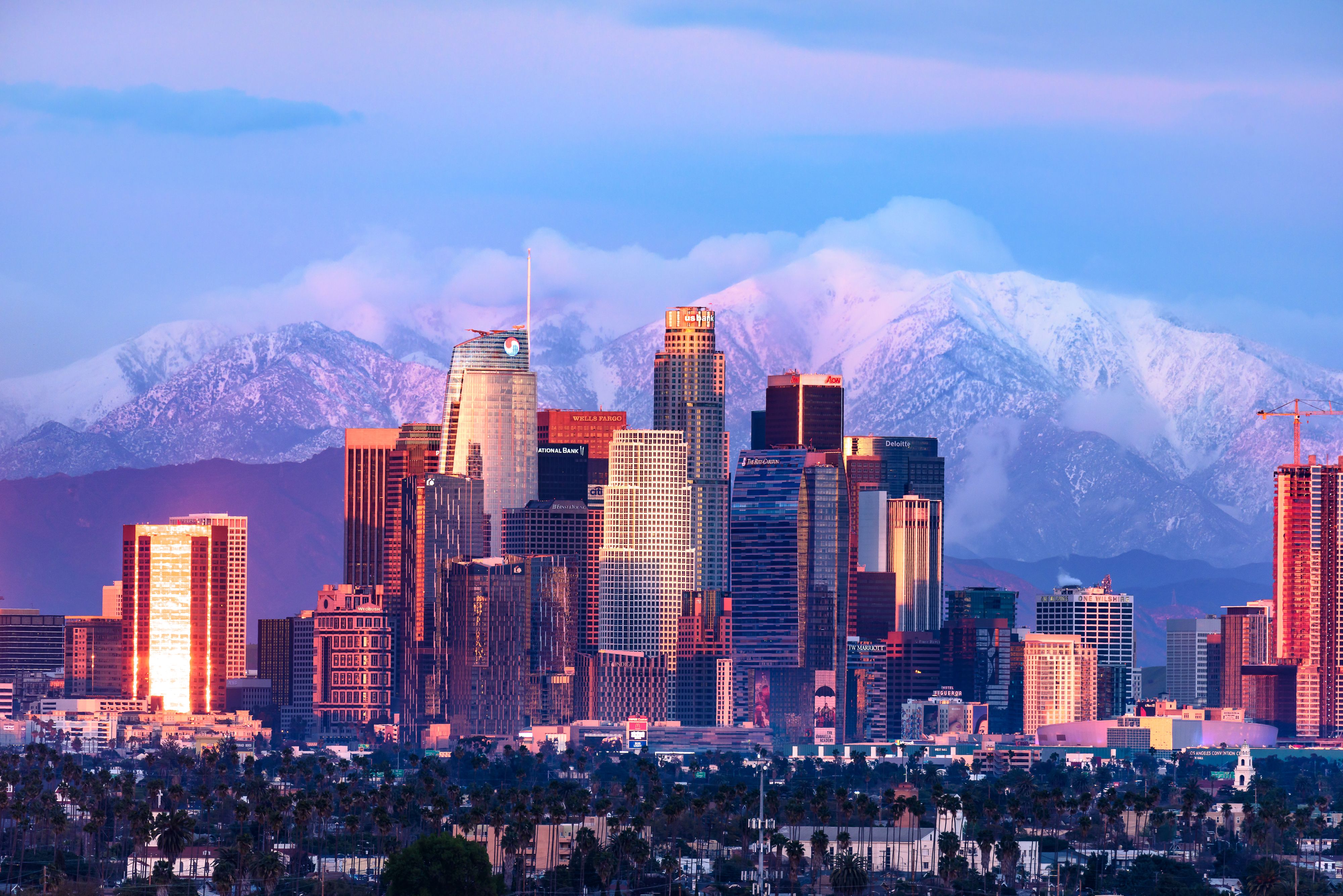 Downtown Los Angeles skyline with snow capped mountains behind at sunset