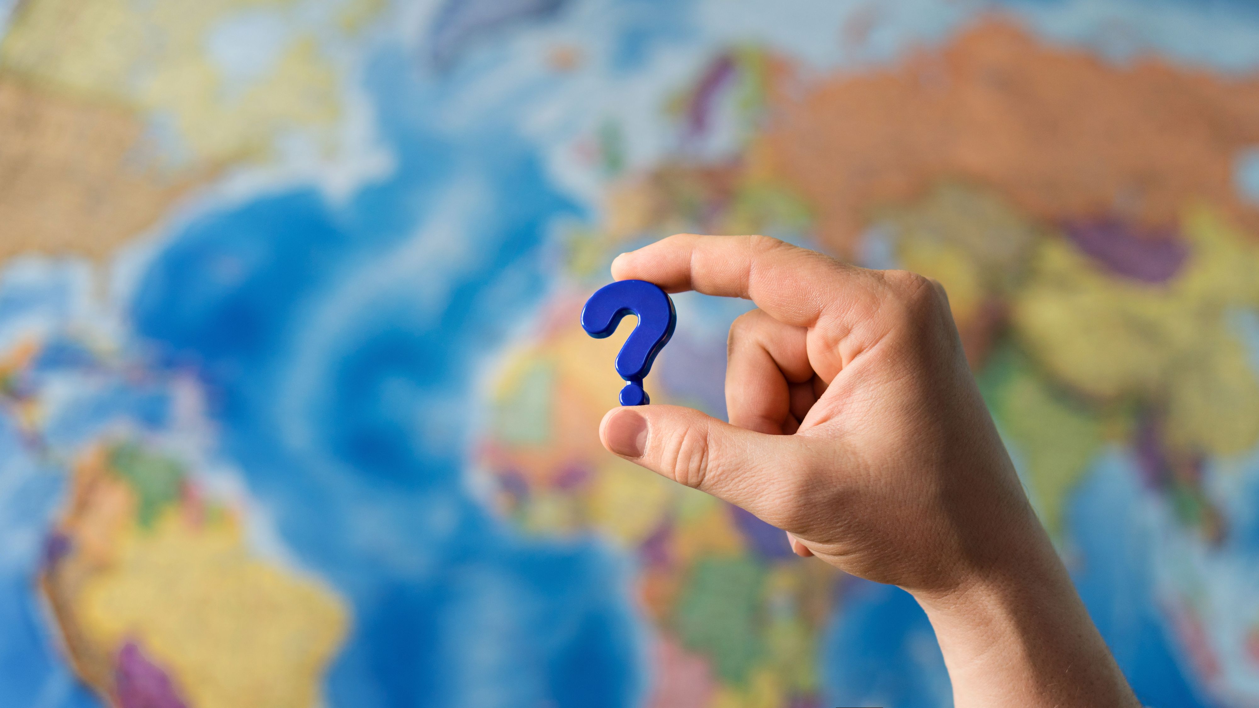 Adult hand holding question mark plastic toy on the world political map background. Travel planning explore destination concept. Quarantine over, borders open
