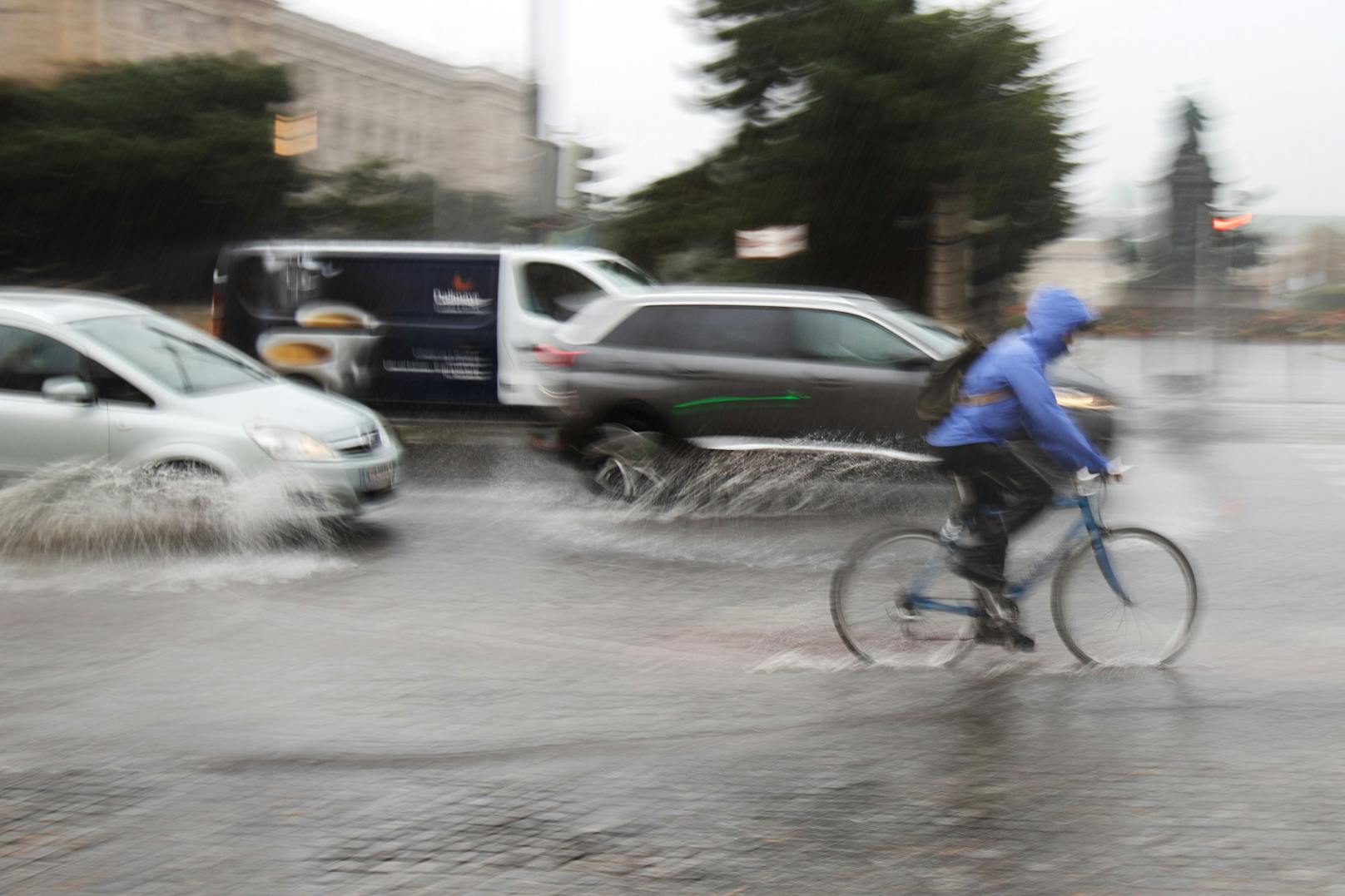 Radfahrer und Autos fahren über eine von starken Regen überflutete Straße am Museumsplatz in Wien. Archivbild