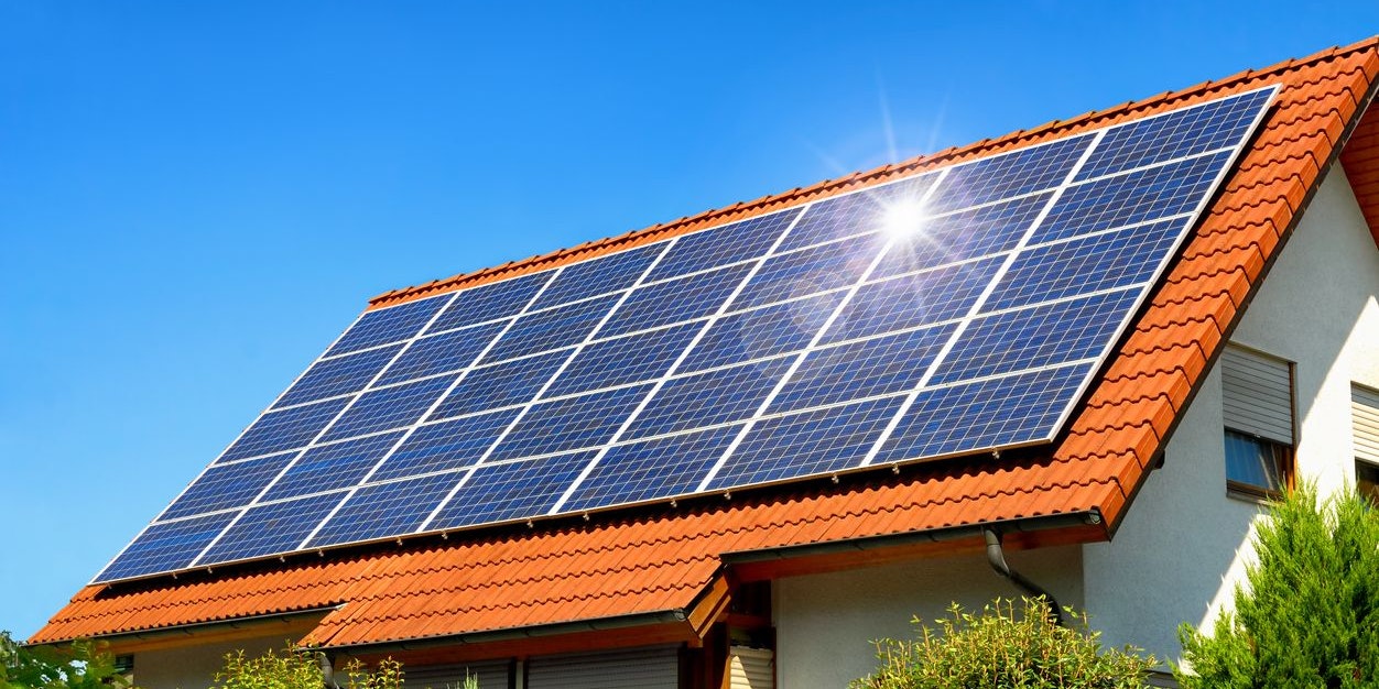 Solar panel on a red roof reflecting the sun and the cloudless blue sky