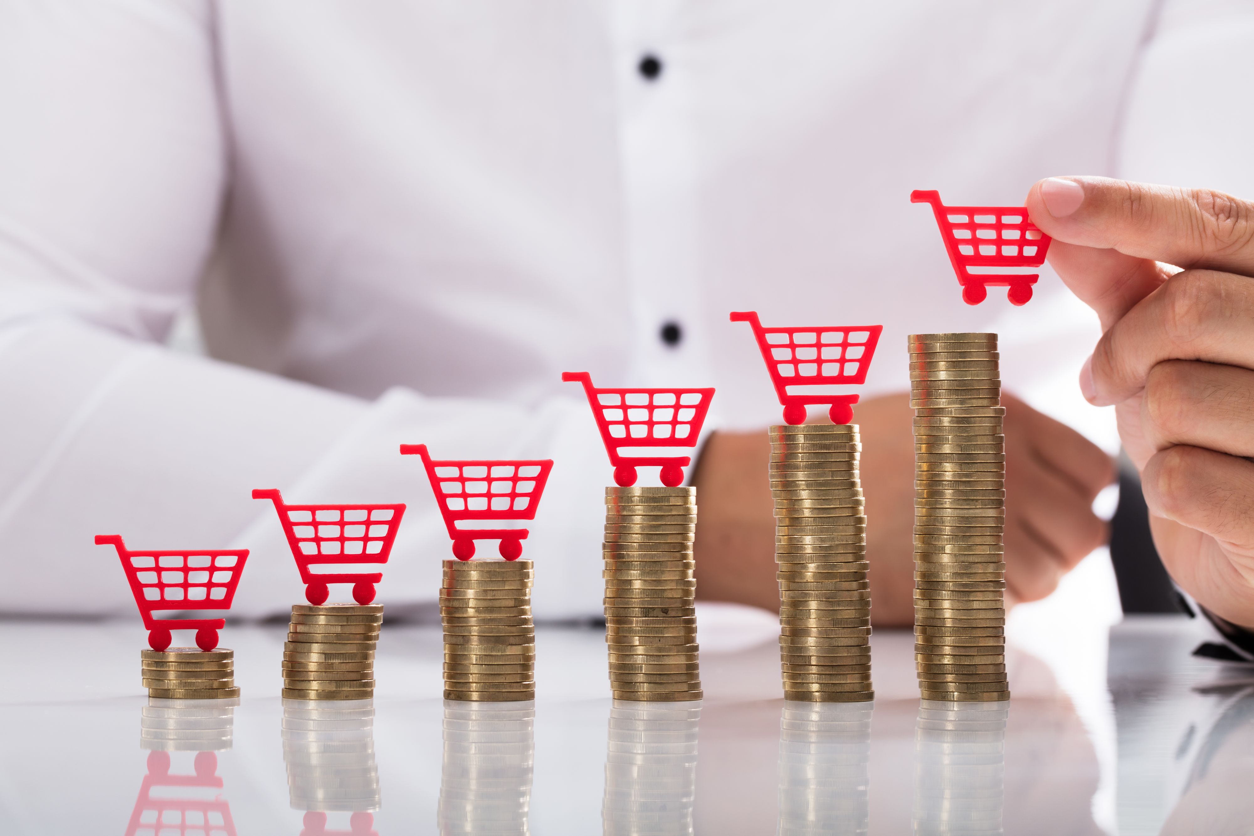 Businessperson's hand placing red shopping cart over increasing stacked coins