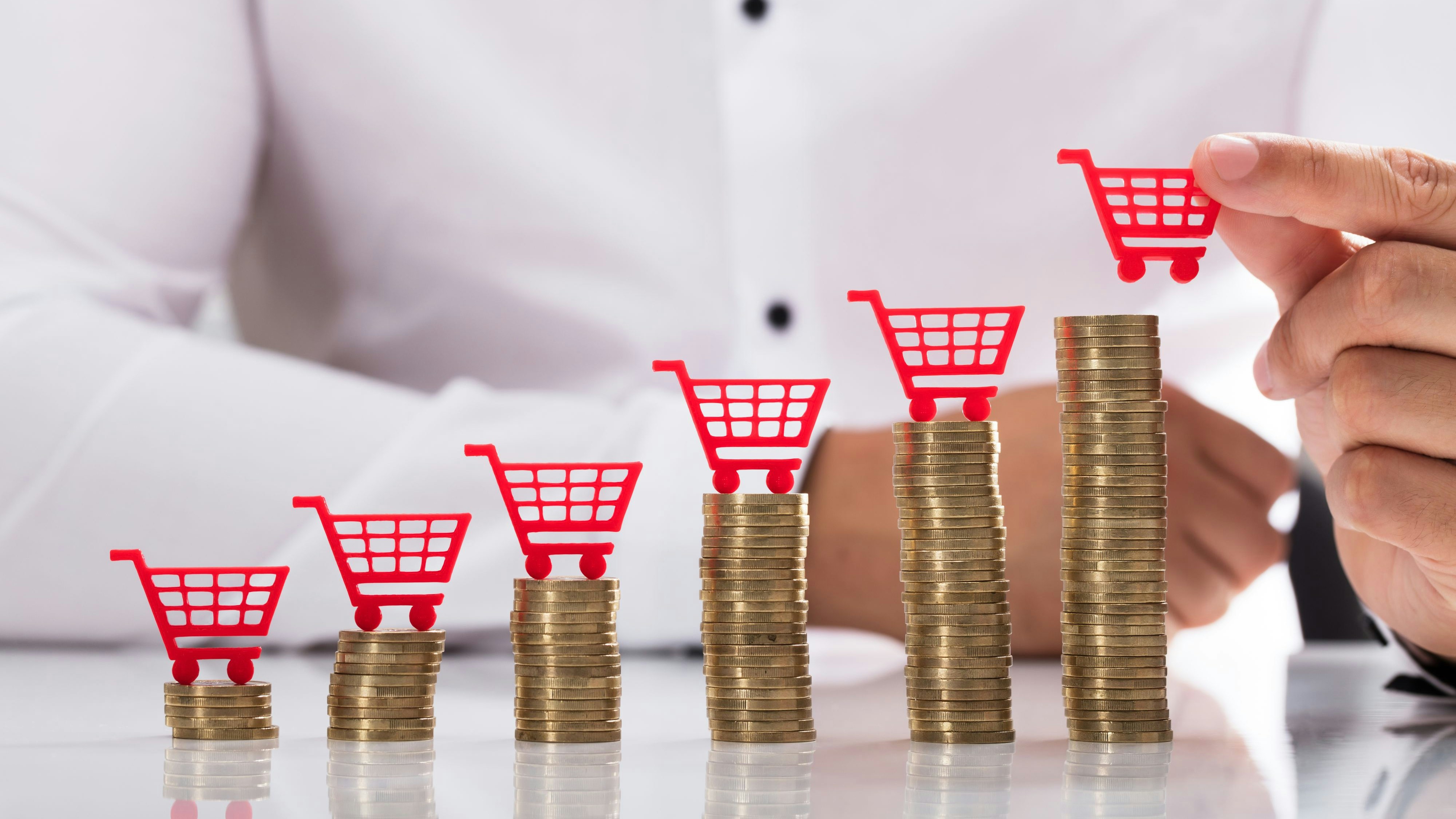 Businessperson's hand placing red shopping cart over increasing stacked coins