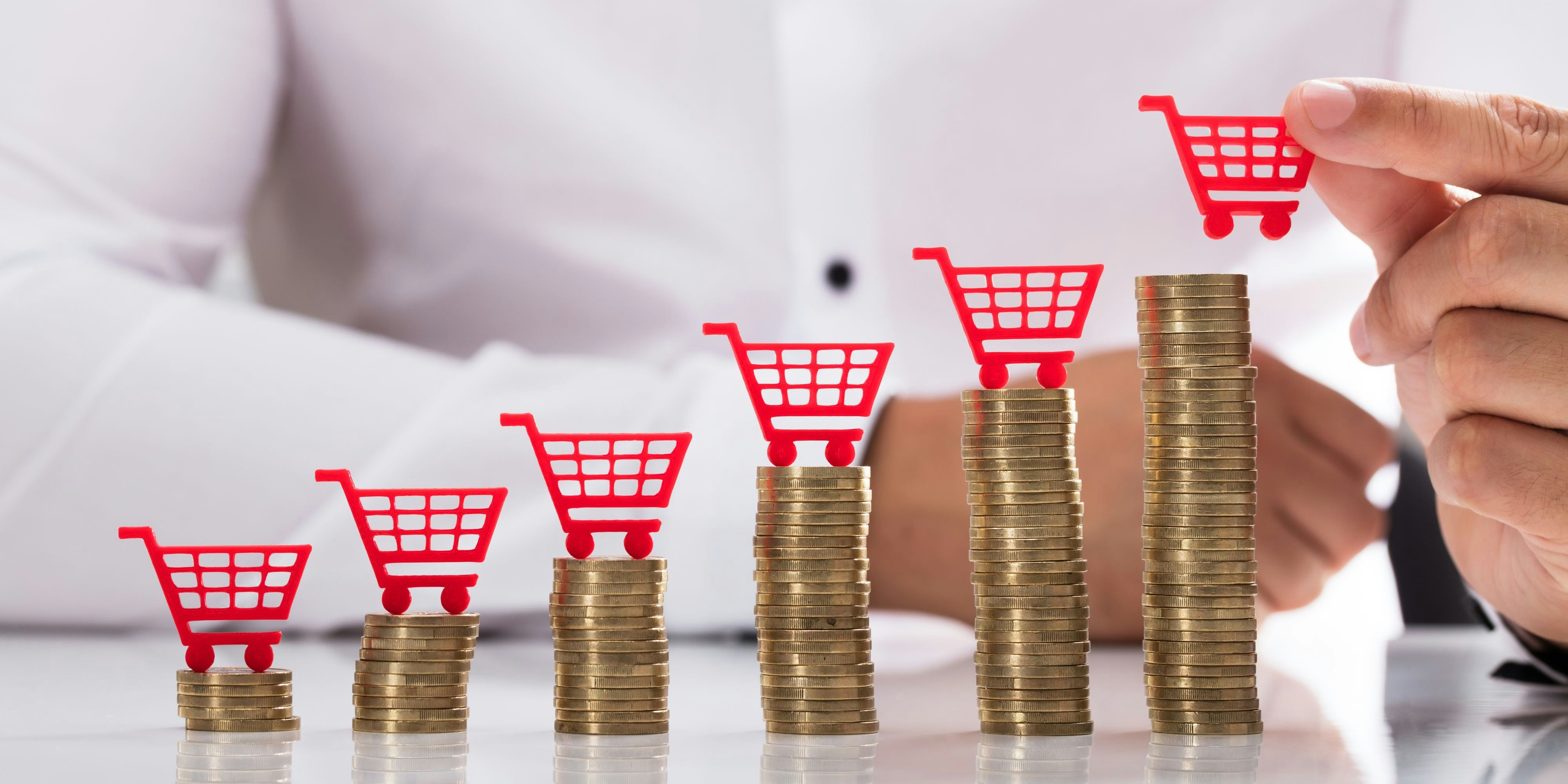 Businessperson's hand placing red shopping cart over increasing stacked coins
