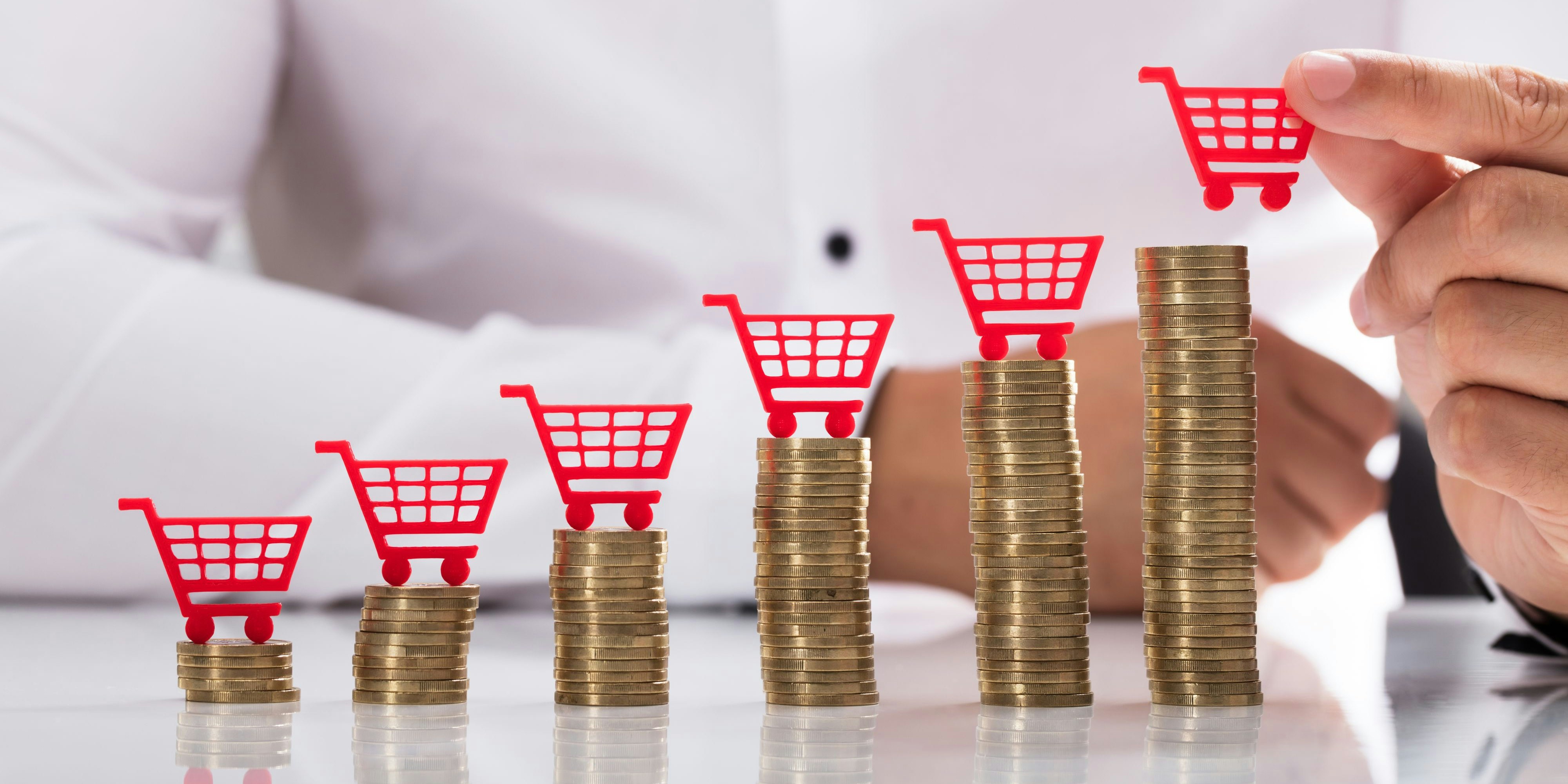 Businessperson's hand placing red shopping cart over increasing stacked coins