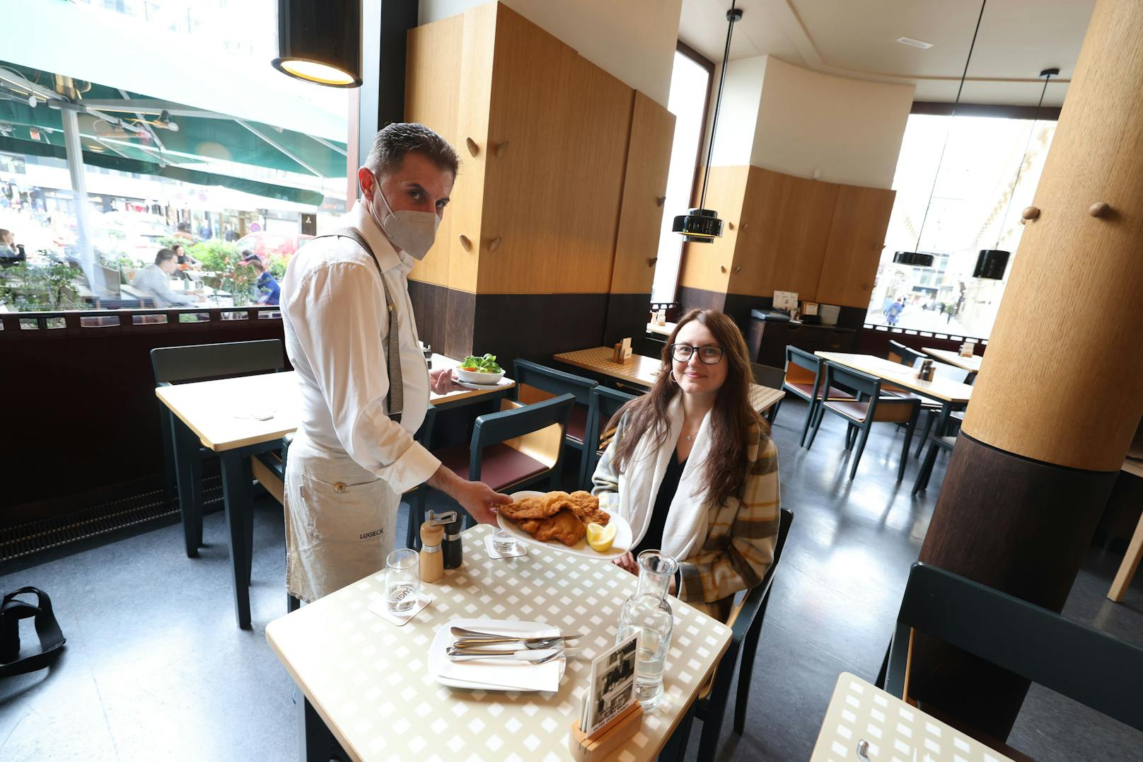 Kellner mit Maske serviert ein Wiener Schnitzel.