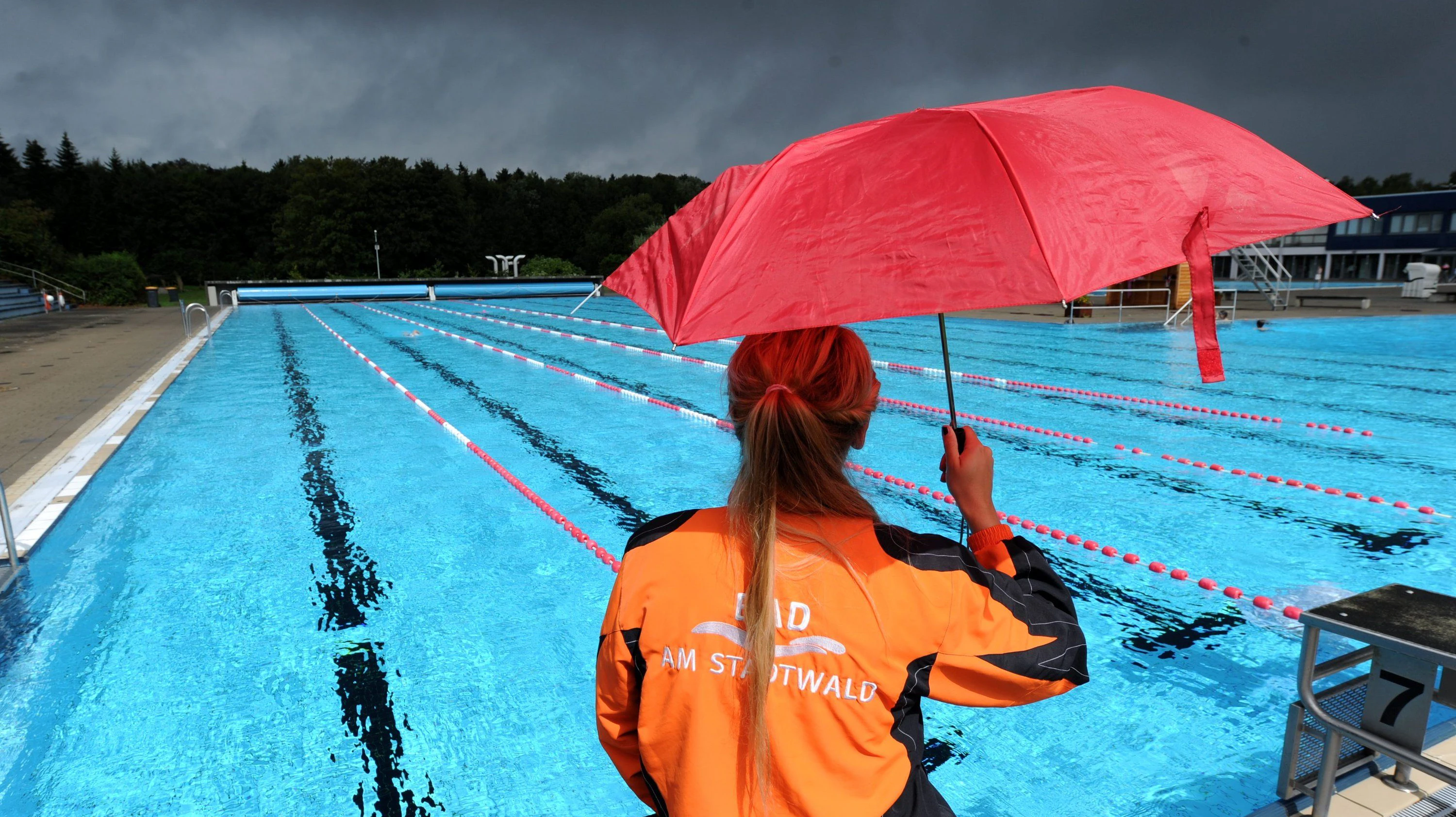 Eine Aufsichtsperson wacht in einem Freibad über den Pool: Bei Regen gibt es kaum Gäste