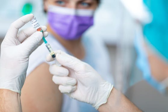 Doctor's hands in surgical gloves pulling COVID-19 vaccine liquid from vial to vaccinate female patient