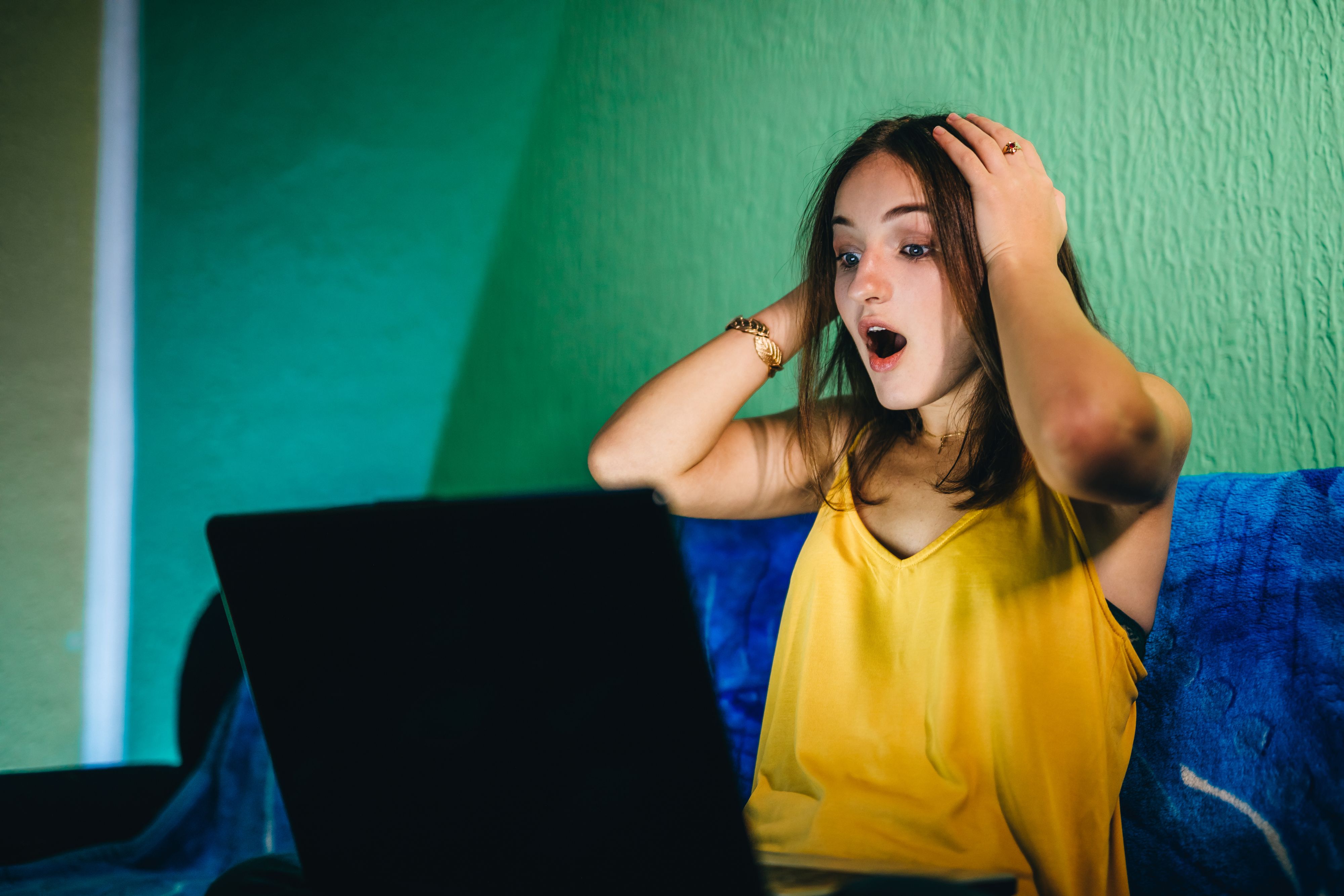 Shocked young Caucasian cute woman using computer at night. Chatting, reading, watching movie or having a video chat with friends.