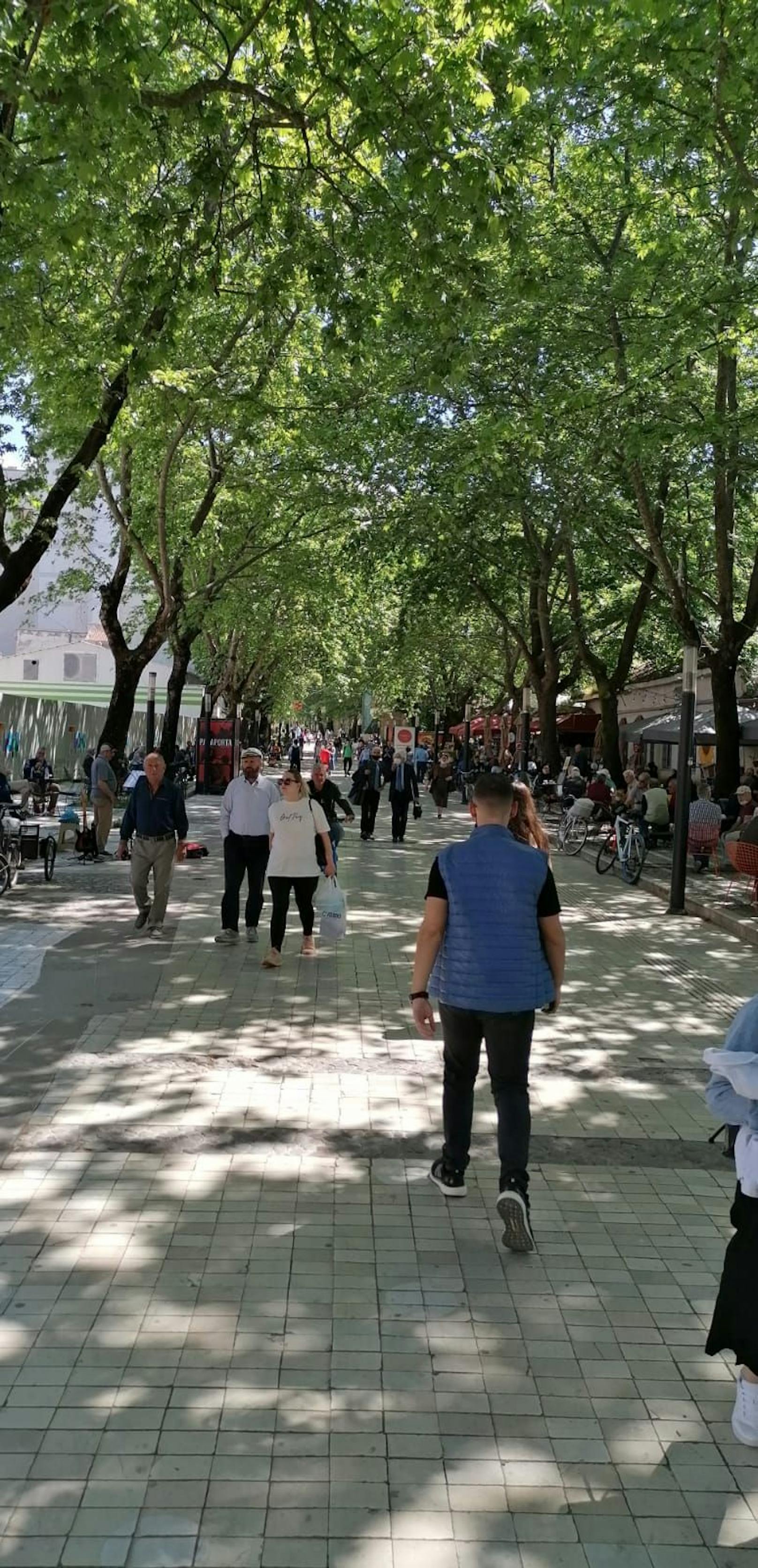 Eine belebte Promenade in Tirana. Die Menschen genießen das Wetter. 