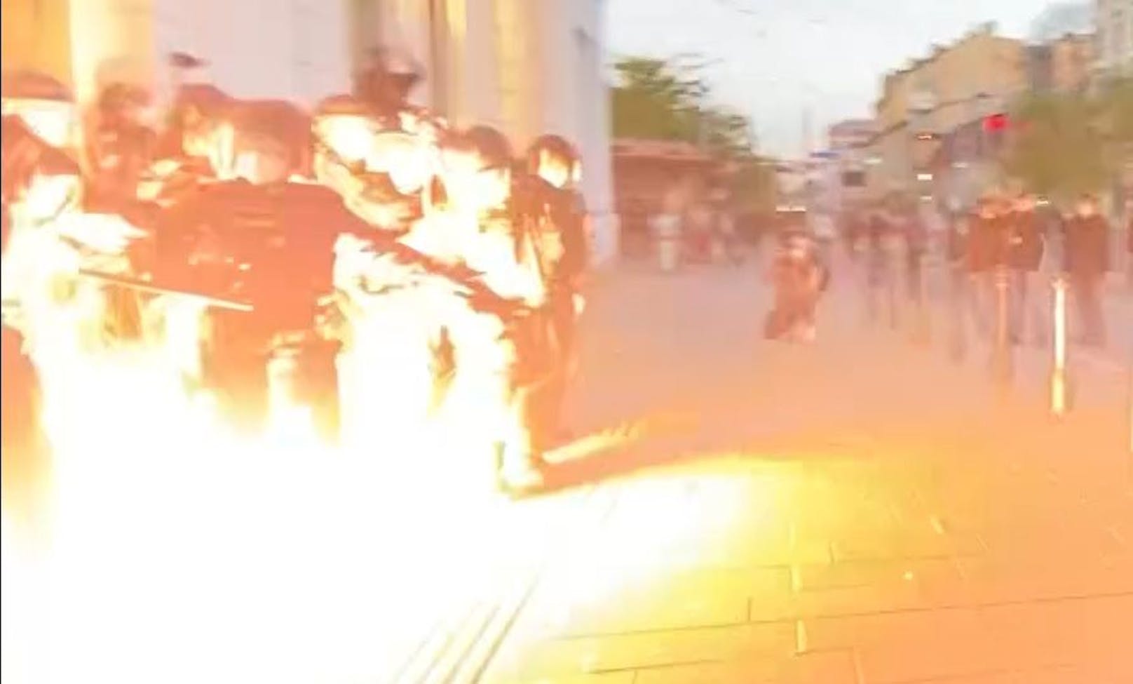 Die Szene zeigt einen explodierenden pyrotechnischen Gegenstand, der auf die Polizei geworfen wurde.