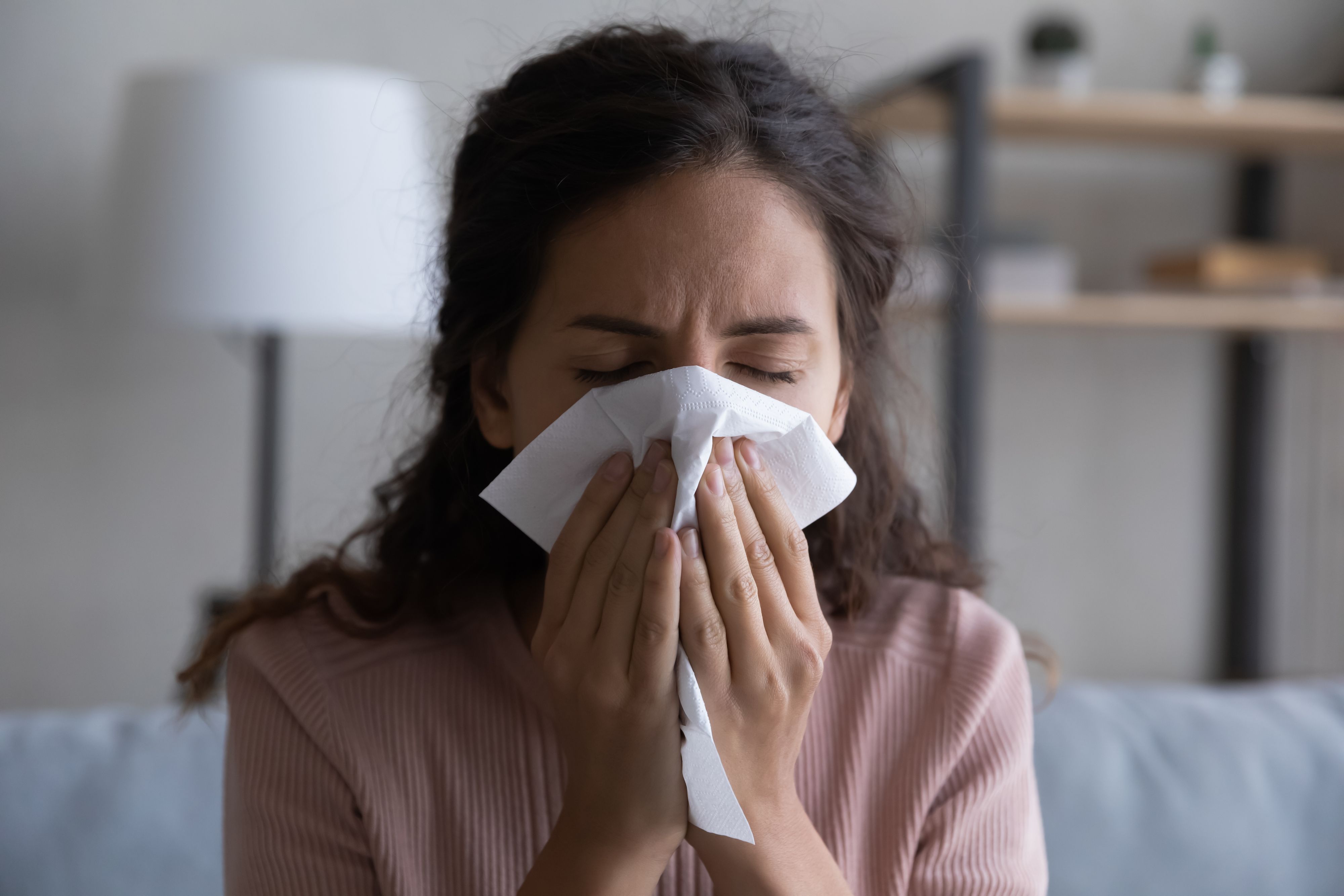 Close up sick woman blowing running nose, sneezing, holding white paper tissue handkerchief, unhealthy young female feeling unwell, symptom of chronic sinusitis, cold or flu, seasonal allergy