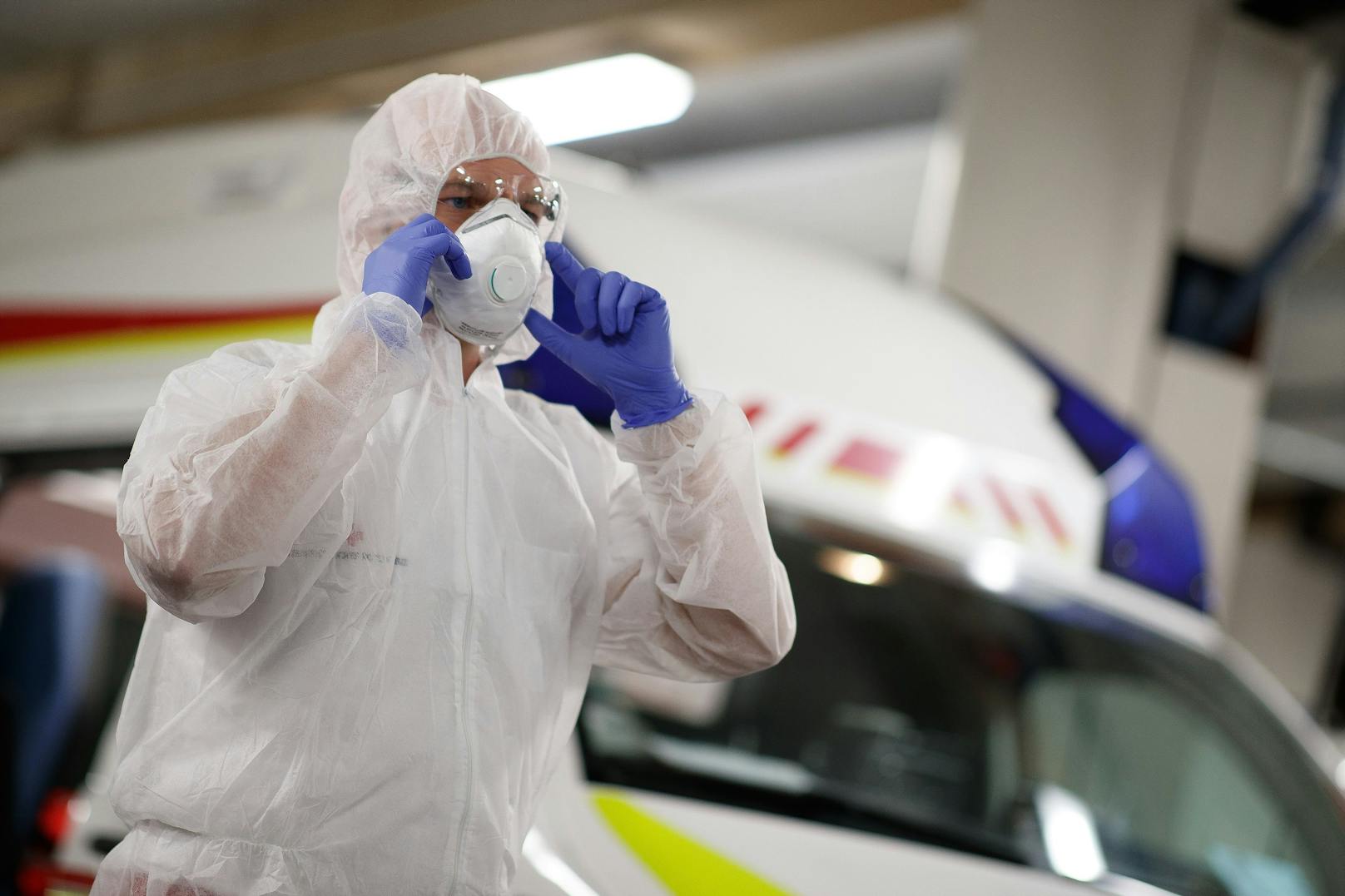 Ein Mitarbeiter des Roten Kreuz beim Anlegen von Handschuhen, Schutzbrille, Schutzmaske und Schutzanzug, um eine Ansteckung mit dem Corona-Virus zu verhindern. Symbolbild