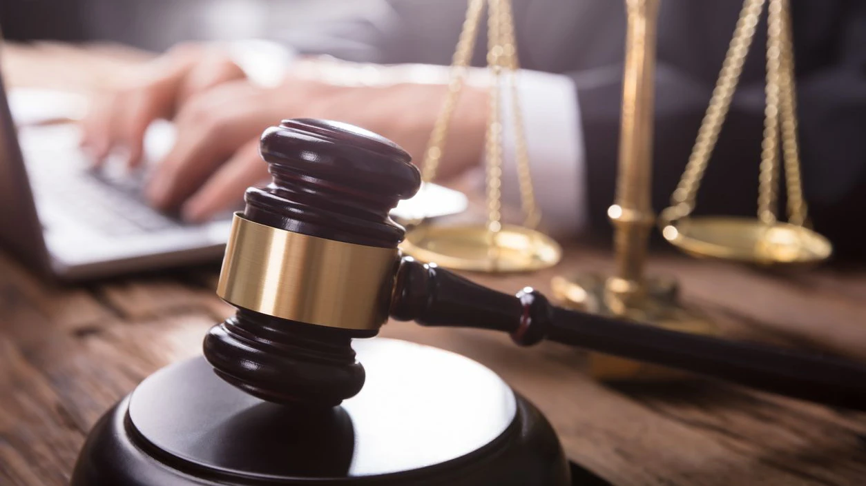 Close-up Of Gavel And Justice Scale In Front Of Judge Using Laptop