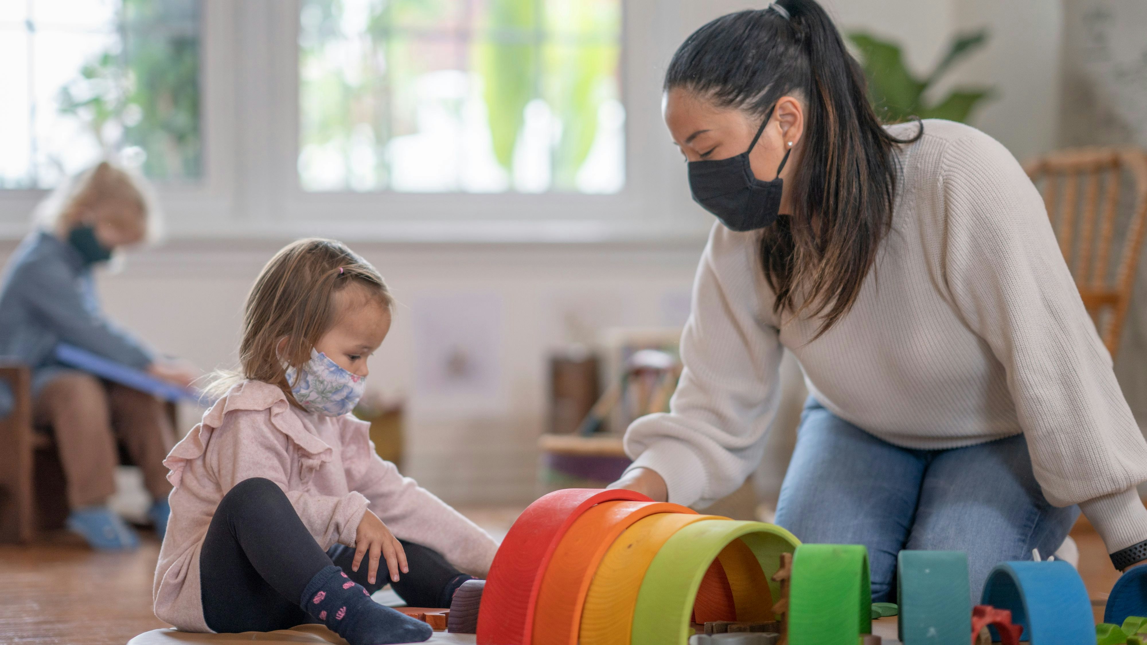 Young girl playing on a play mat at daycare while wearing a mask due to COVID-19.