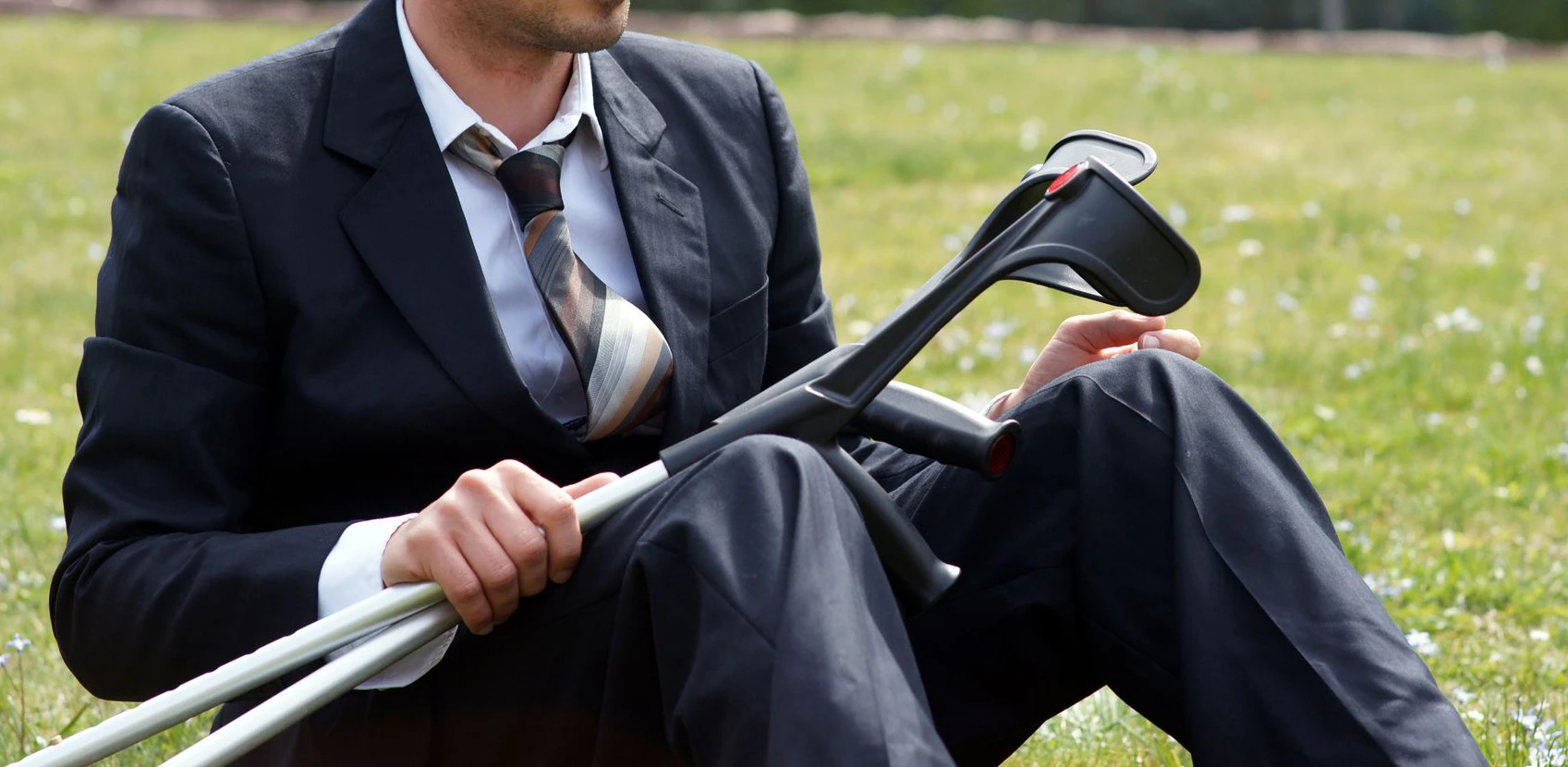 Ein Mann sitzt mit einer Krücke im Park. Symbolbild