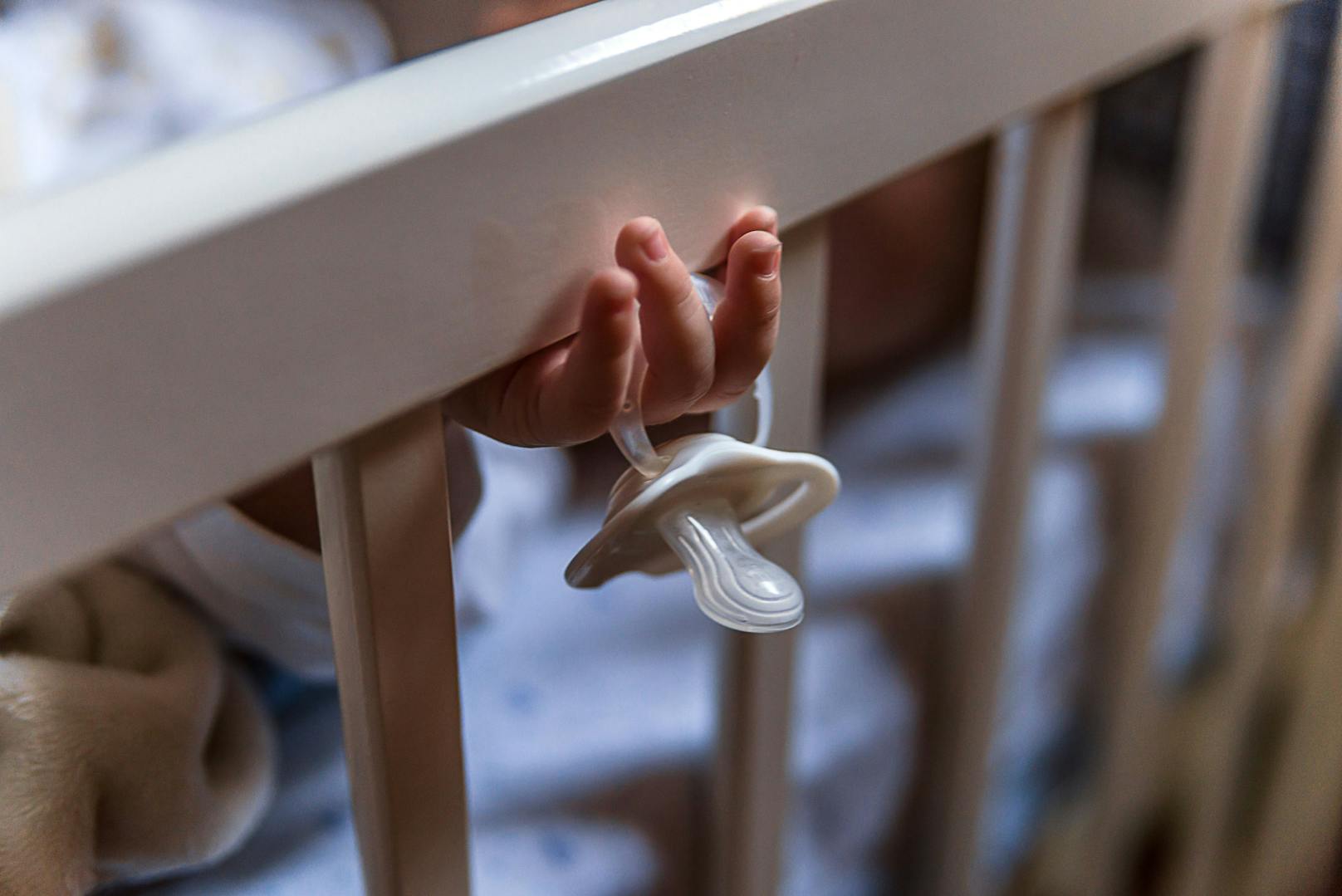 Ein schlafendes Baby in einem Kinderbett hält einen Schnuller. Symbolbild