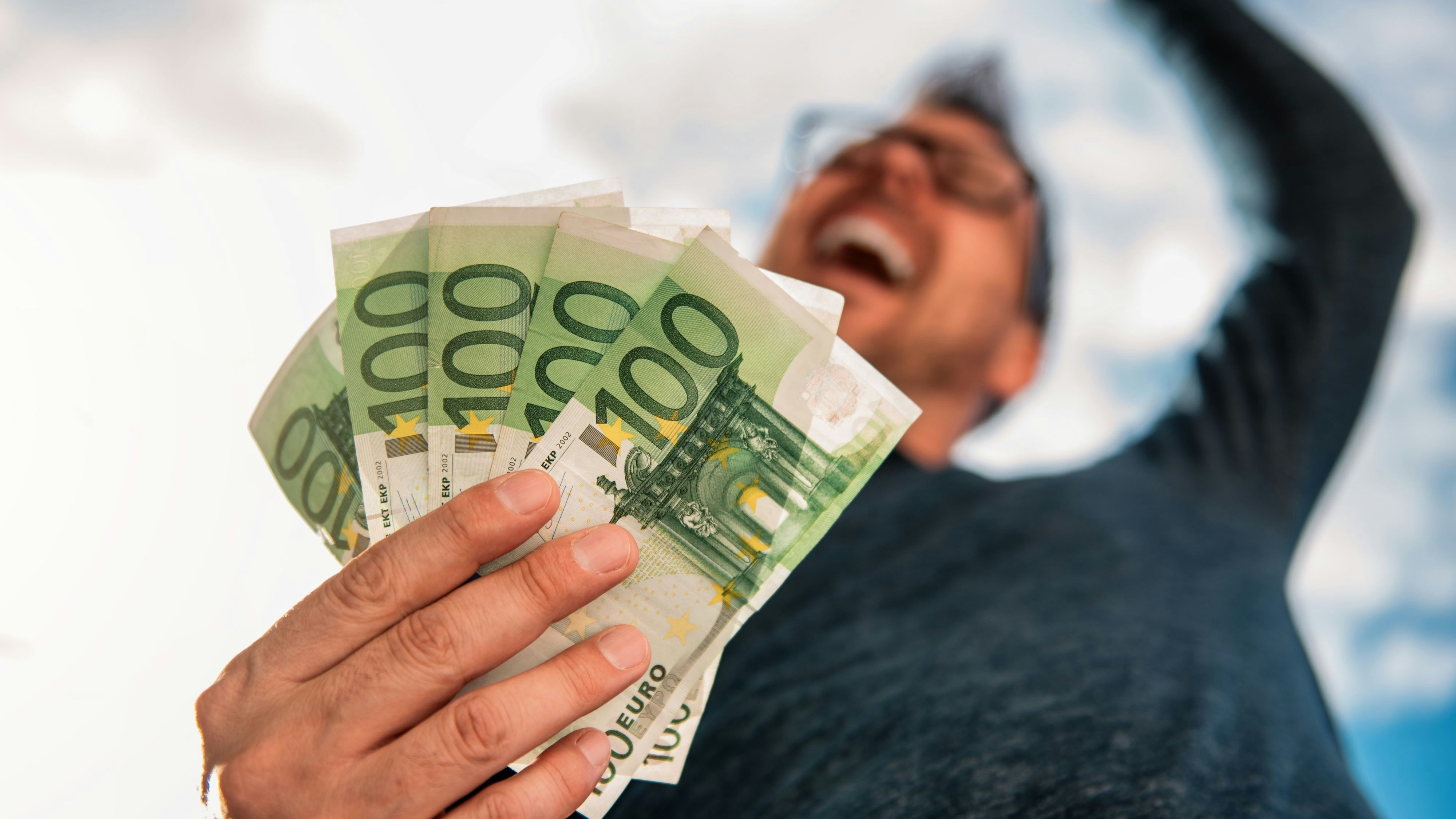 Man with glasses wearing blue shirt. and holding stack of money.