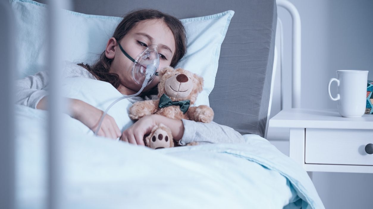 Kid with cystic fibrosis lying in hospital bed with oxygen mask and plush toy