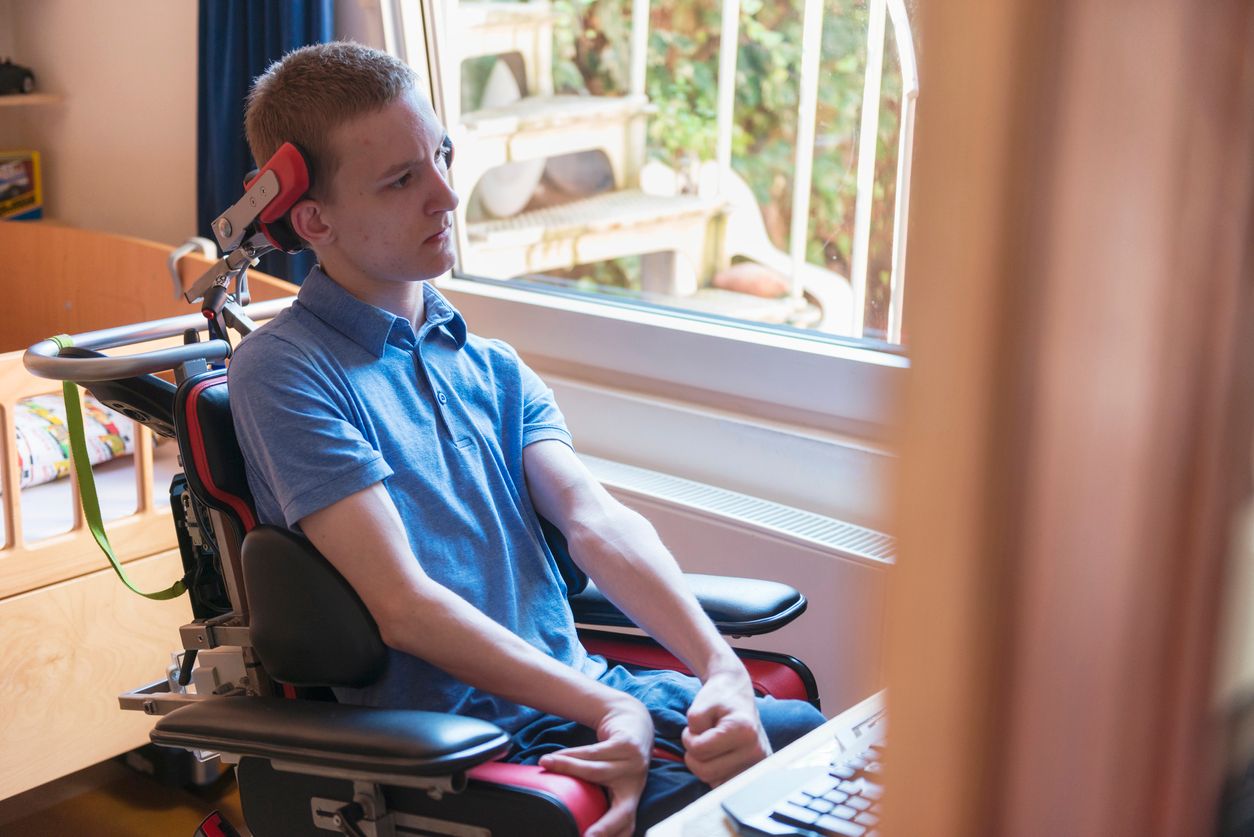 Color image of a real life young physically impaired ALS patient computer gaming with the help of his electronic wheelchair.