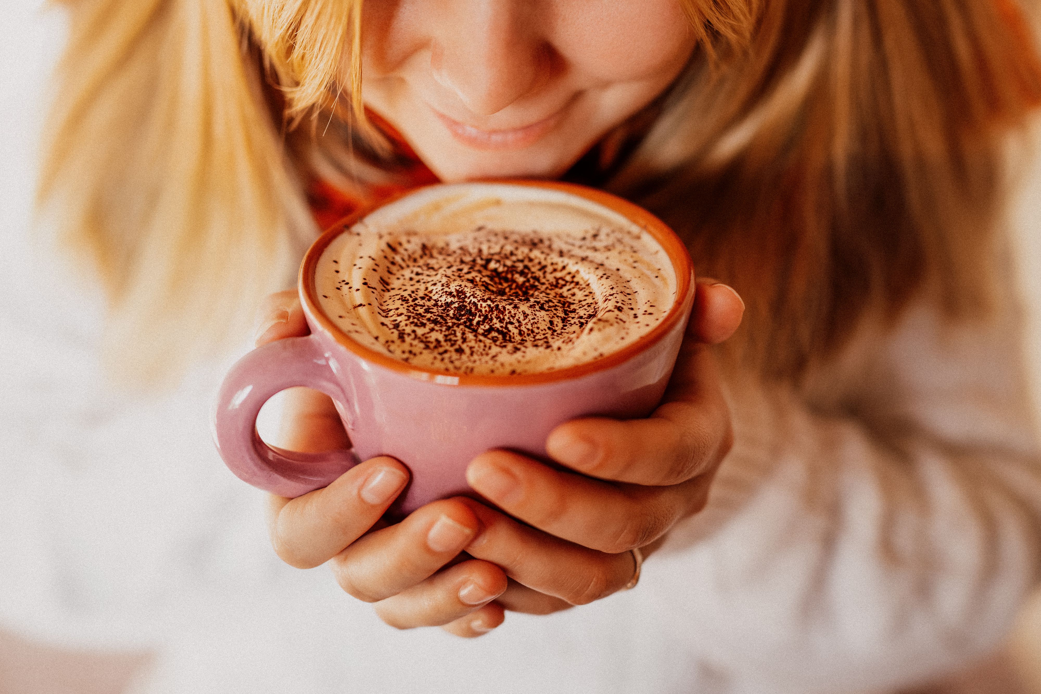Young woman with a white winter pullover holding in her hands her creamy sunday morning coffee. Taken directly from above. Selective focus. Grain added. Part of a series.