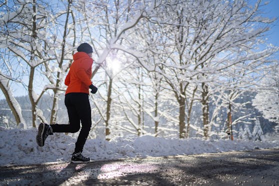 Eine Frau joggt bei Sonnenschein durch eine verschneite Winterlandschaft. (Symbolbild)