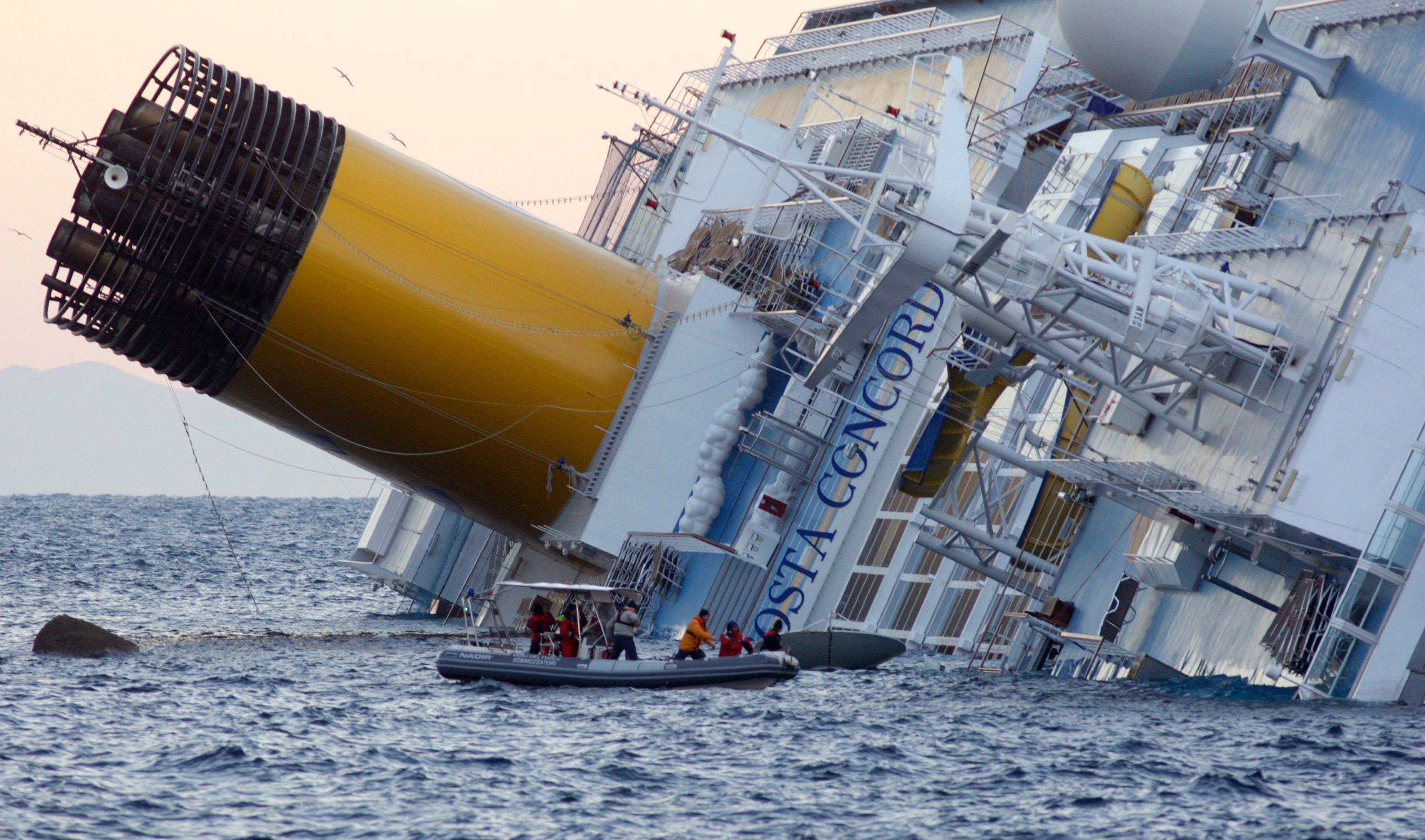 Rescuers stand in a boat next to the Costa Concordia cruise ship that ran aground off the west coast of Italy, at Giglio island January 15, 2012. At least three people were killed after the Italian cruise ship with more than 4,000 on board capsized, running aground and keeling over in shallow waters.  REUTERS/Remo Casilli  (ITALY - Tags: TRANSPORT DISASTER TPX IMAGES OF THE DAY)