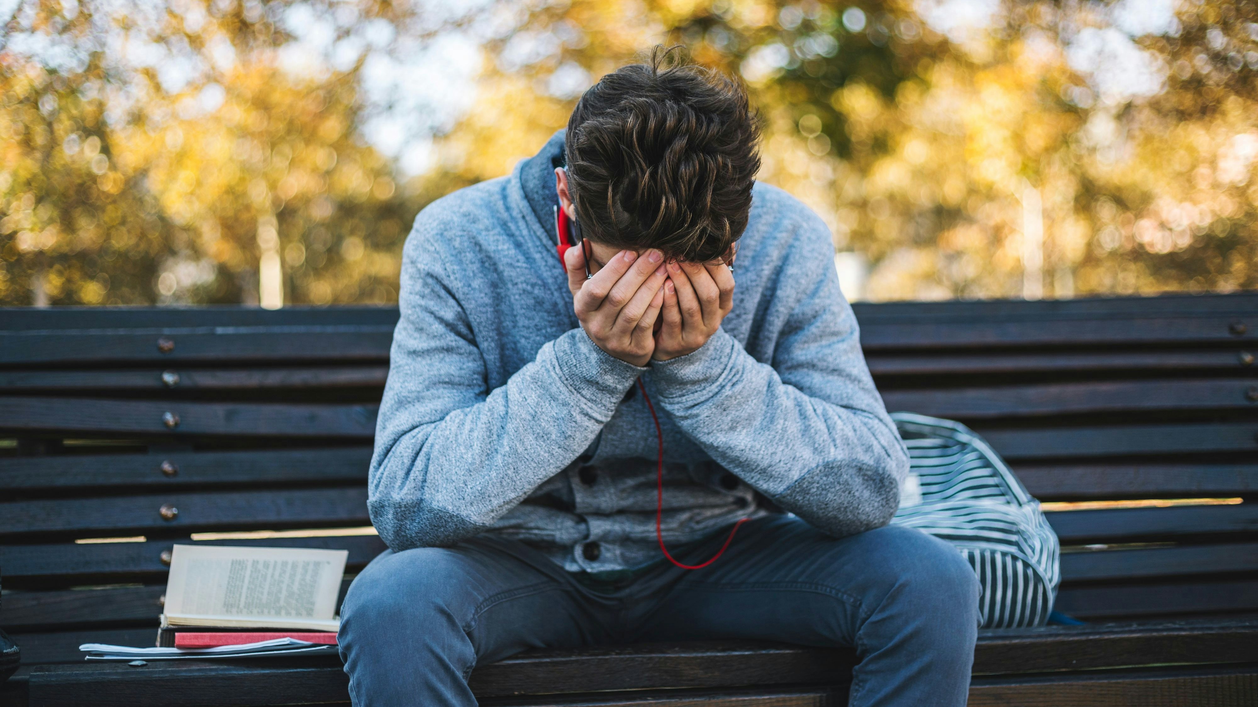 Teenager sits on a bench in the park and listen to music and learning for exame