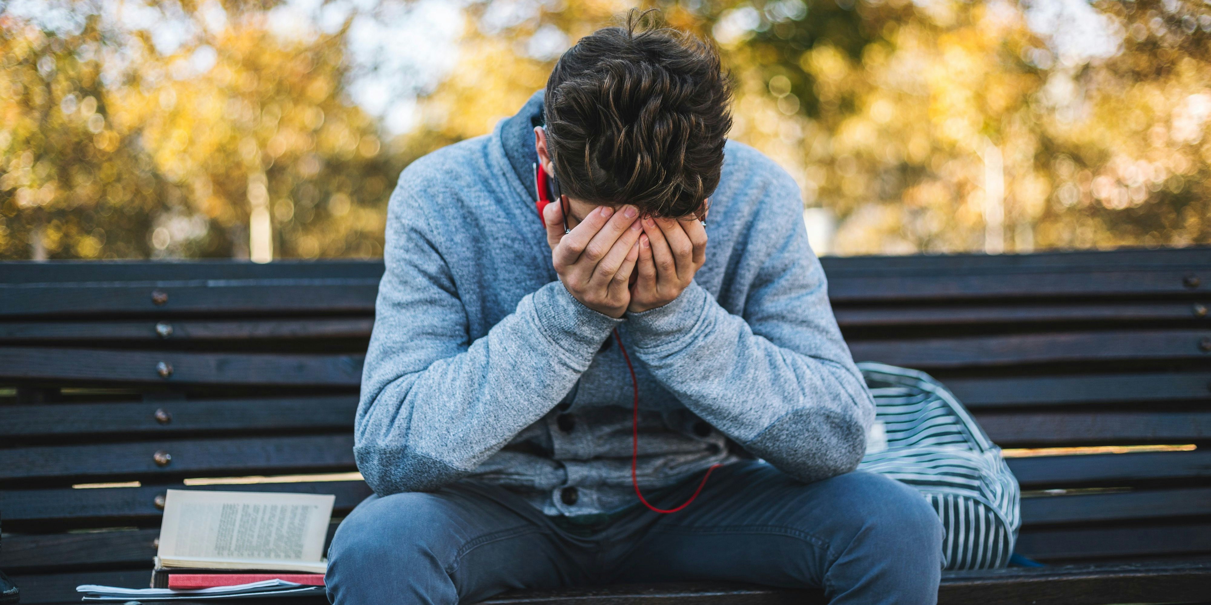 Teenager sits on a bench in the park and listen to music and learning for exame