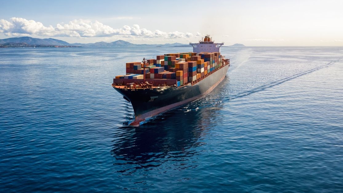 Aerial view of a heavy loaded container cargo vessel traveling over calm, blue sea