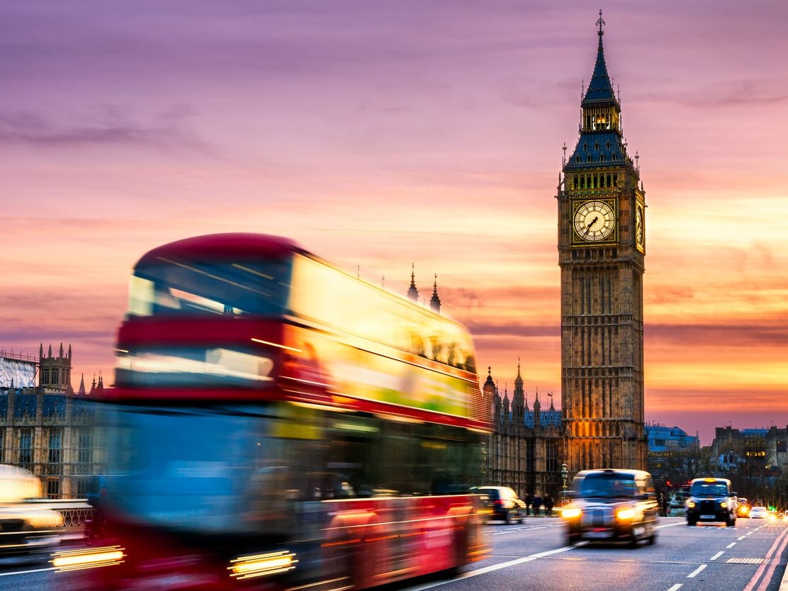 Big Ben with the Houses of Parliament and a red double-decker bus passing at dusk