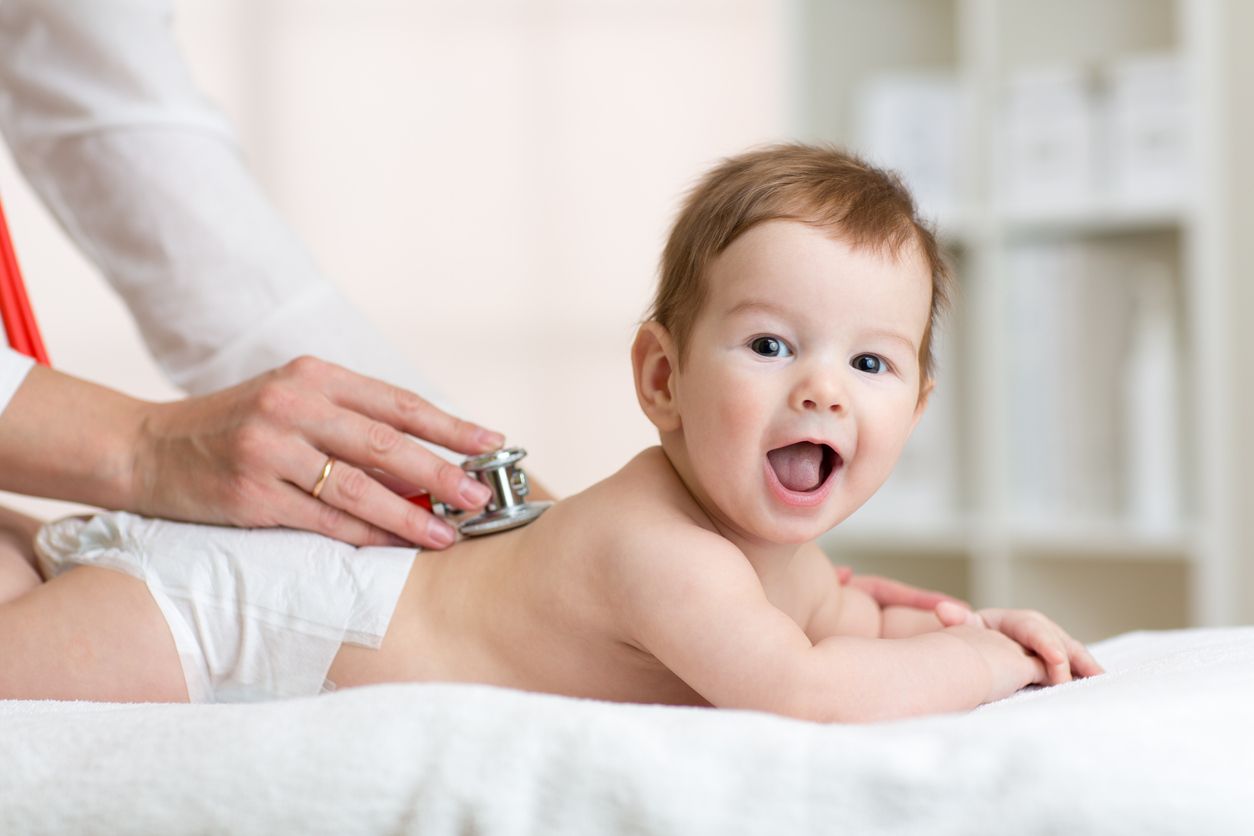 Pediatrician examining baby boy. Doctor using stethoscope listen to kid back checking heart beat.