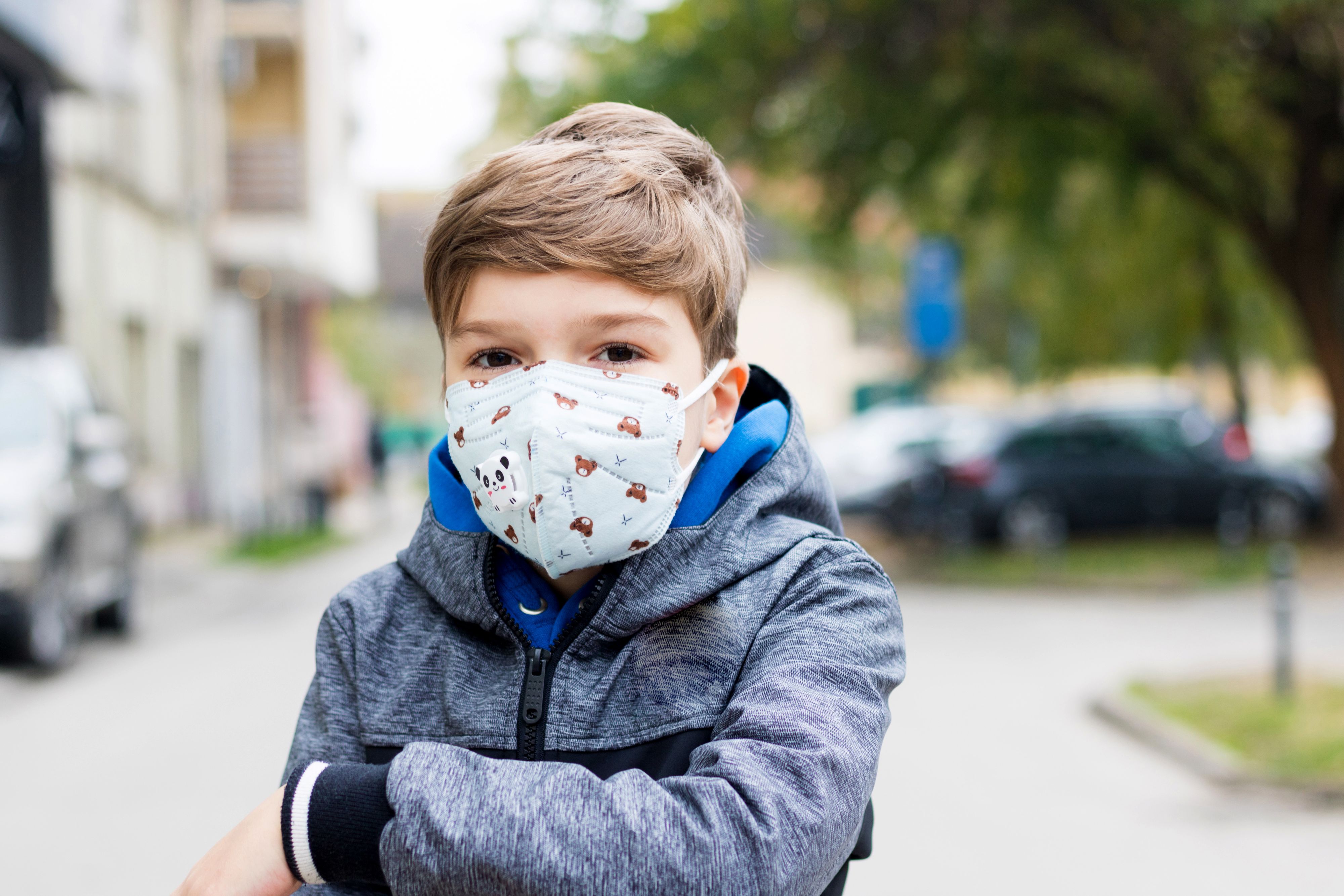 Portrait of a boy wearing protective face mask outdoors during coronavirus pandemic and looking at camera.