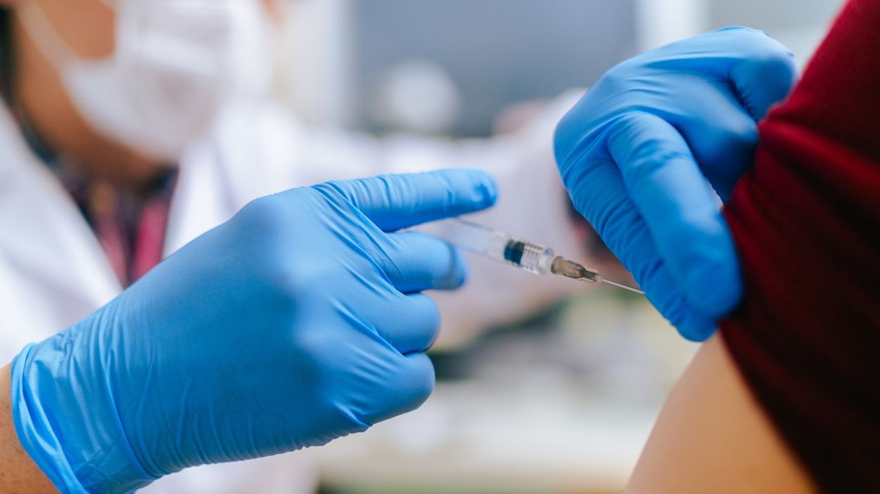 A woman is getting vaccinated by a senior adult doctor in his doctor`s office.