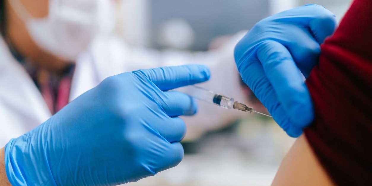 A woman is getting vaccinated by a senior adult doctor in his doctor`s office.