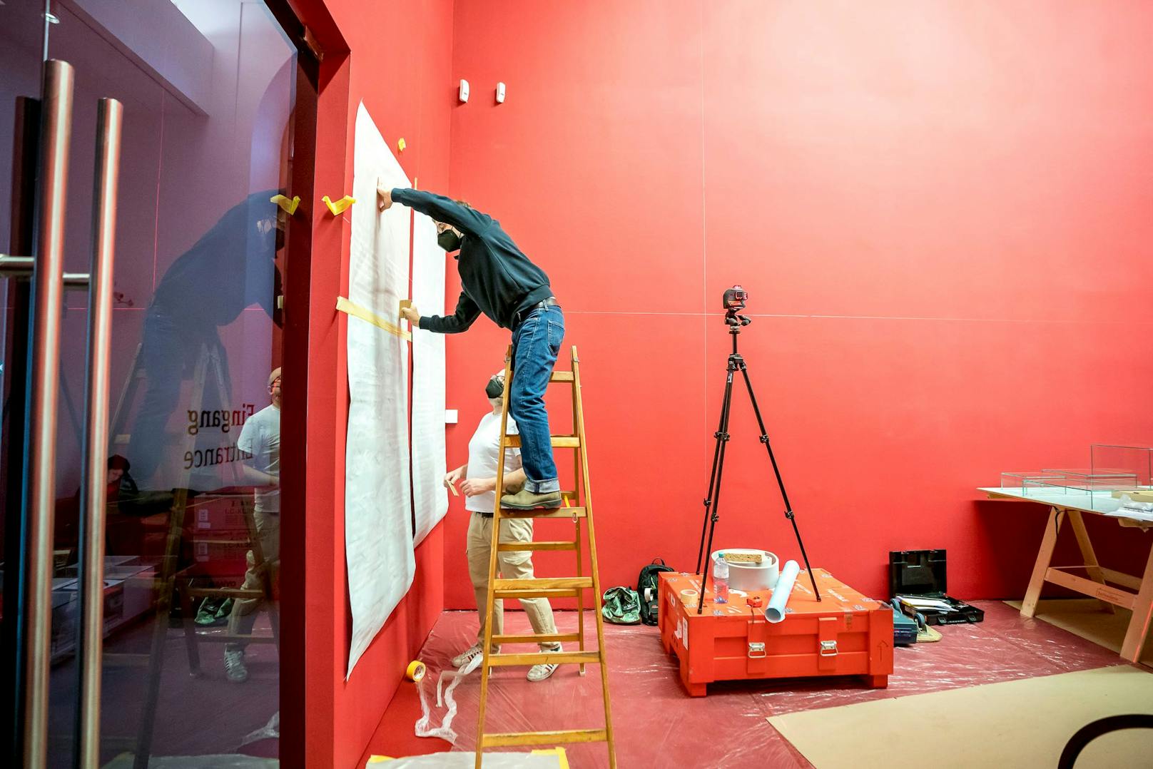 Der Ausstellungstext wird an den roten Wänden links und rechts angebracht.