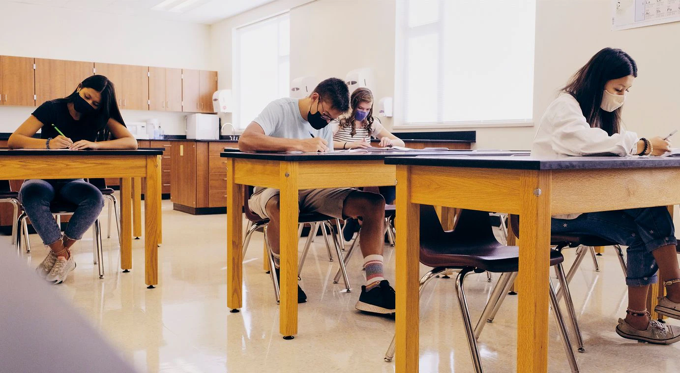 High school students in a classroom, wearing protective face masks to help against spreading infectious disease.