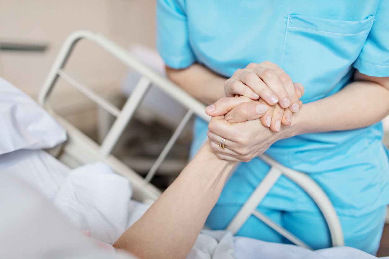 Midsection of female nurse holding senior woman's hand. Caring medical professional is with patient. She is consoling elderly woman in hospital.