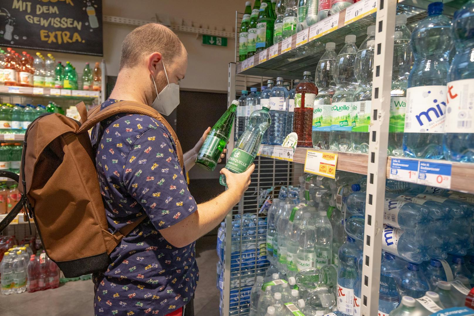Ein Mann vergleicht in einem Supermarkt verschiedene Mineralwasser-Angebote.