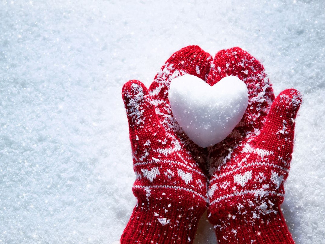 Female hands in knitted mittens with snowy heart against snow background. Love, winter and Valentines day romantic creative concept with copy space for text