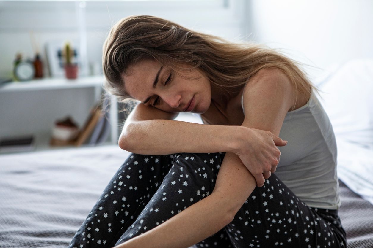 Sad woman looking away while sitting on bed in bedroom