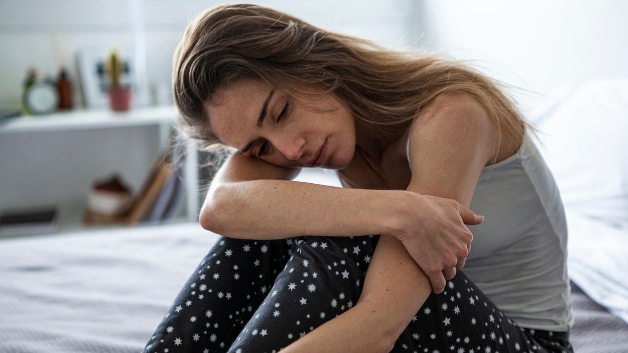 Sad woman looking away while sitting on bed in bedroom