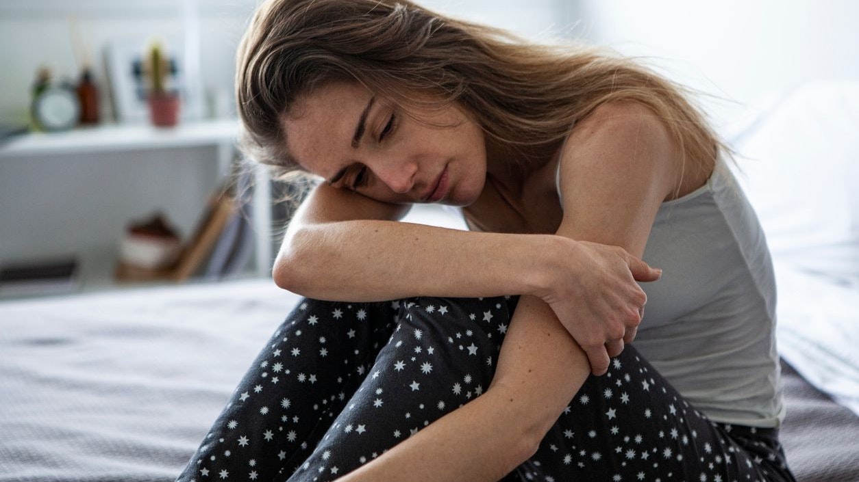 Sad woman looking away while sitting on bed in bedroom