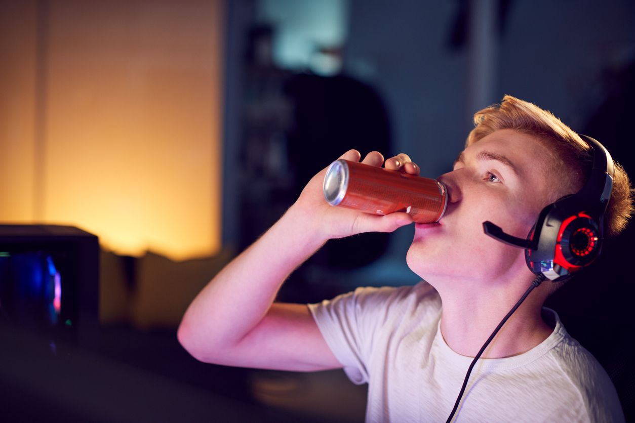 Teenage Boy Drinking Caffeine Energy Drink Gaming At Home Using Dual Computer Screens At Night