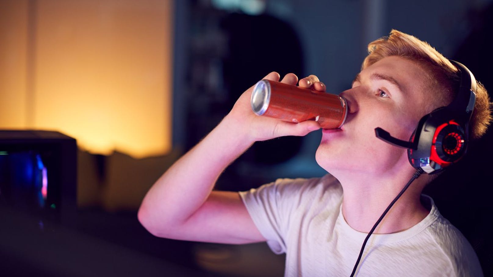 Teenage Boy Drinking Caffeine Energy Drink Gaming At Home Using Dual Computer Screens At Night