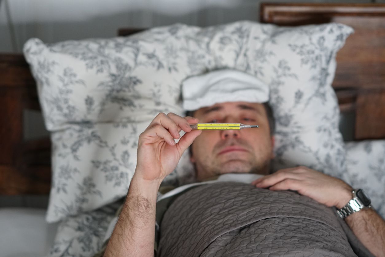 Sick and tired man lying in bed measuring his temperature with a thermometer. Selective focus