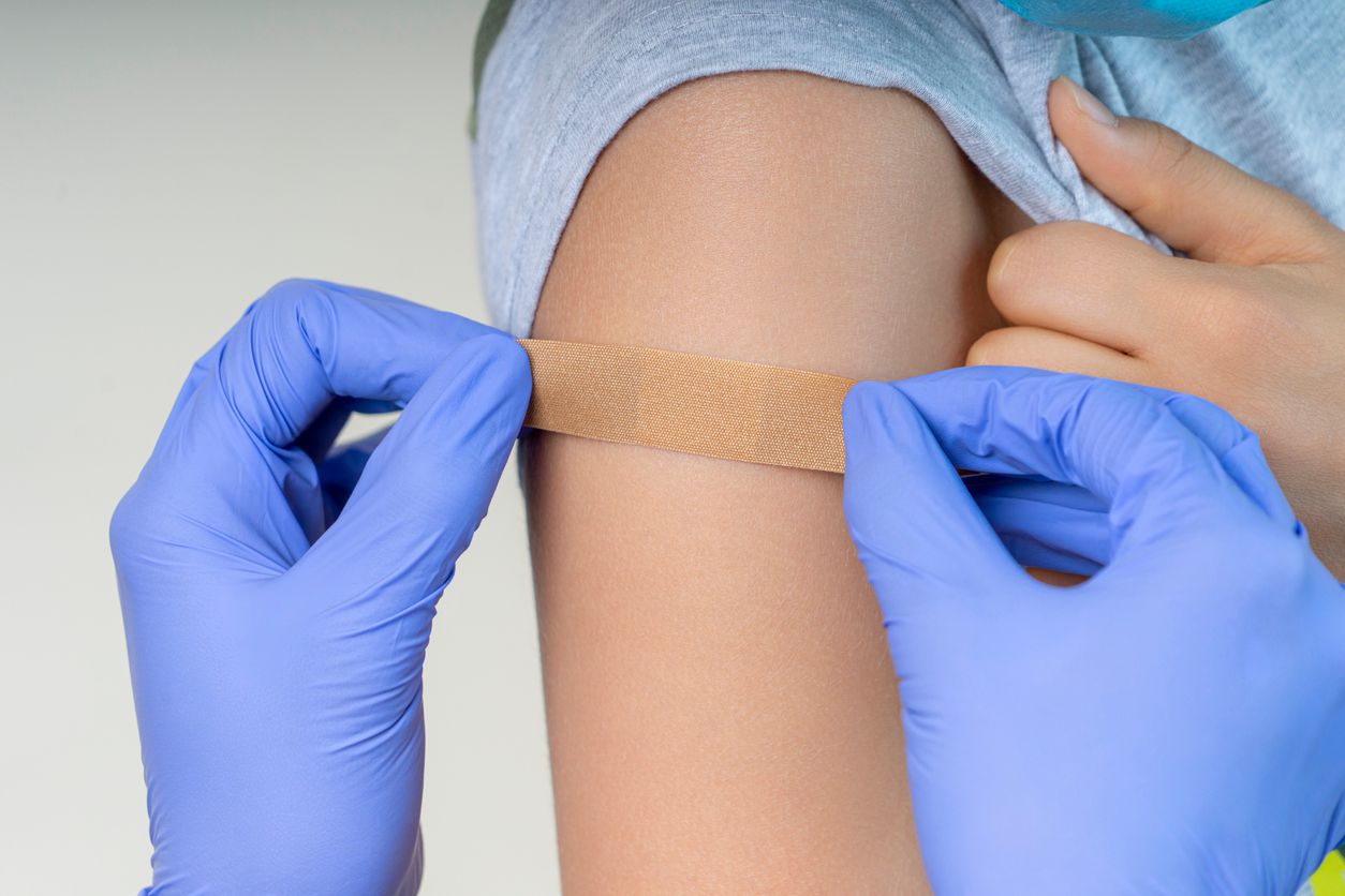 Nurse in rubber protective gloves putting adhesive bandage plaster on teenage boy arm after vaccination. Injection covid vaccine, healthcare for children and teenagers. Close up.
