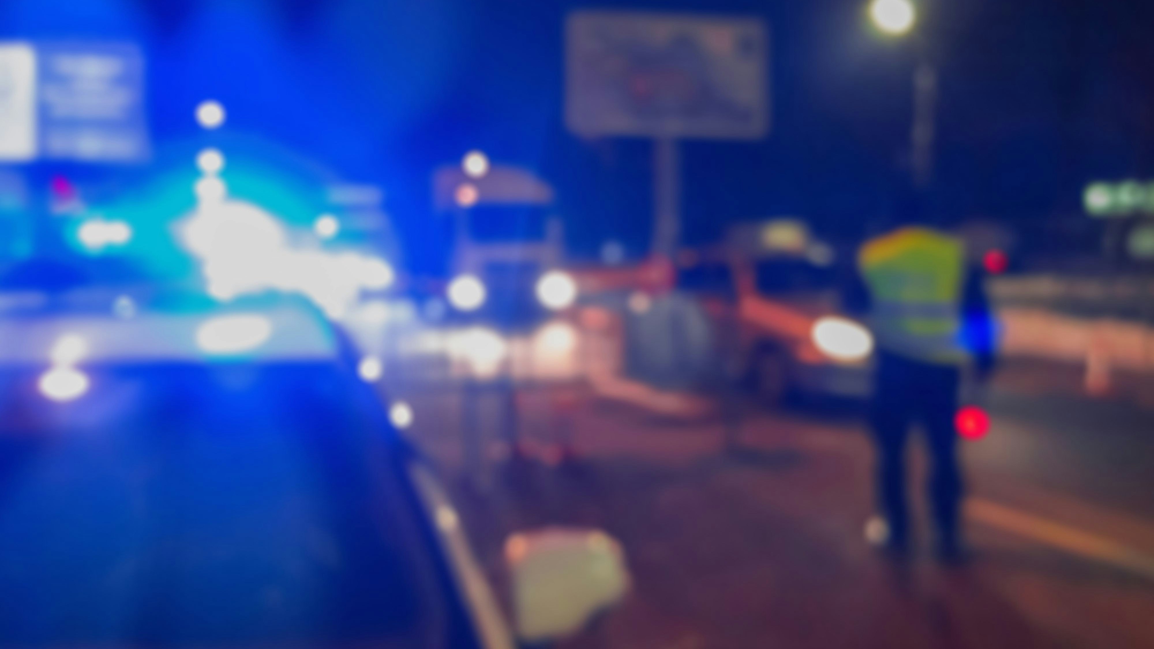 Unrecognizable blurry police car lights and police force officer on night road background, crime scene, night patrolling the city. Abstract blurry image.