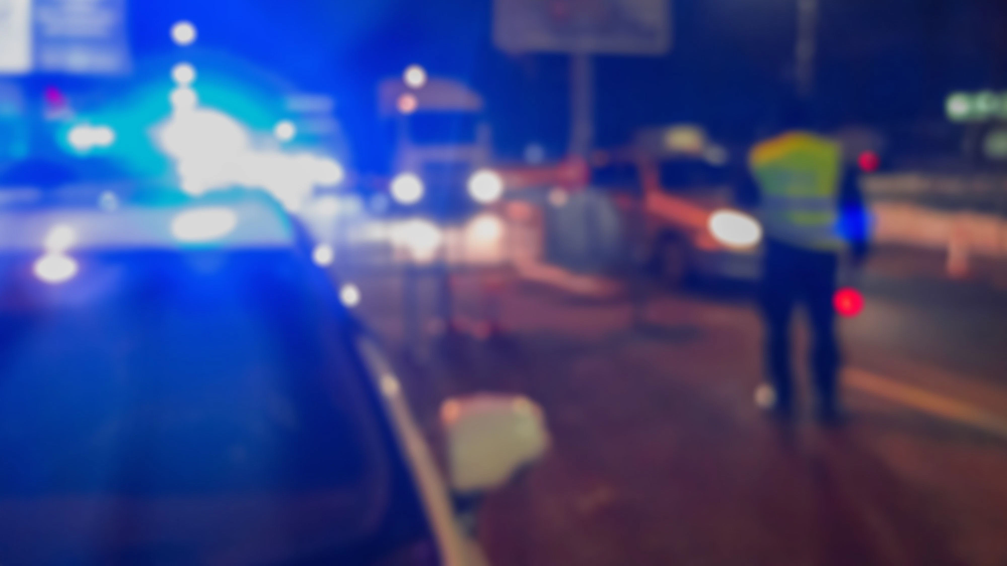 Unrecognizable blurry police car lights and police force officer on night road background, crime scene, night patrolling the city. Abstract blurry image.